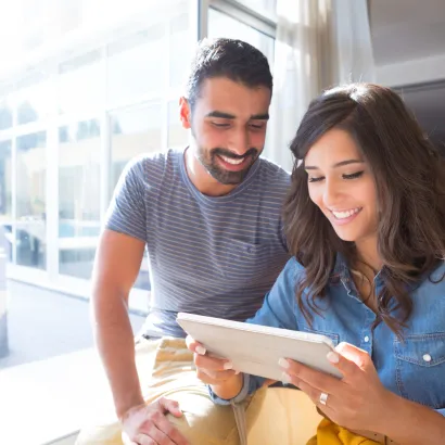 A man and a woman are sitting next to each other looking at a tablet.
