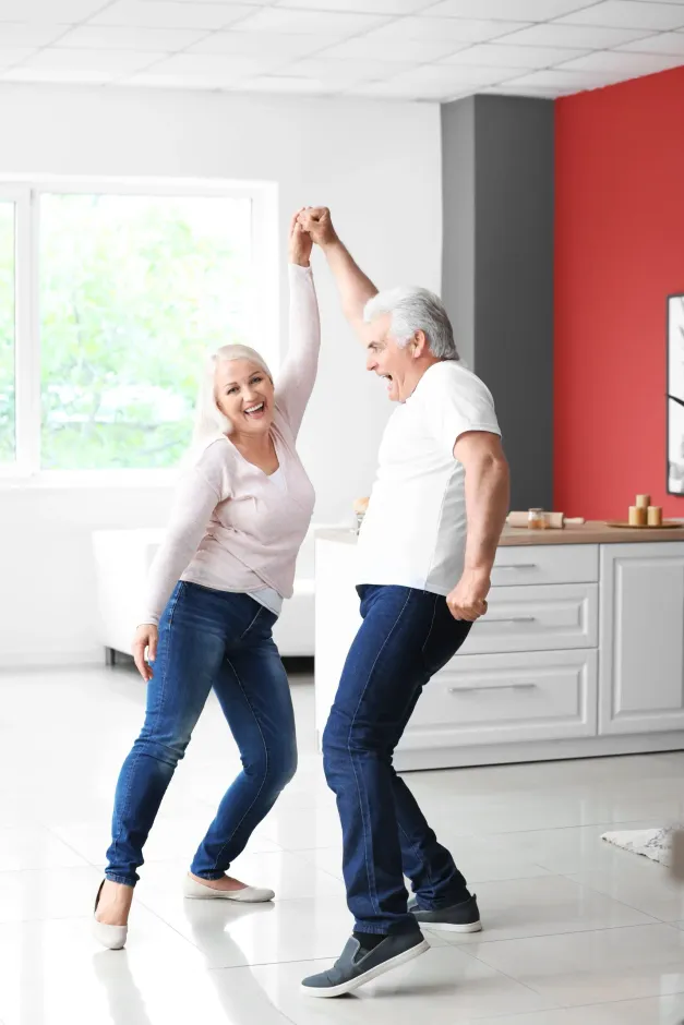 An elderly couple is dancing together in a living room.