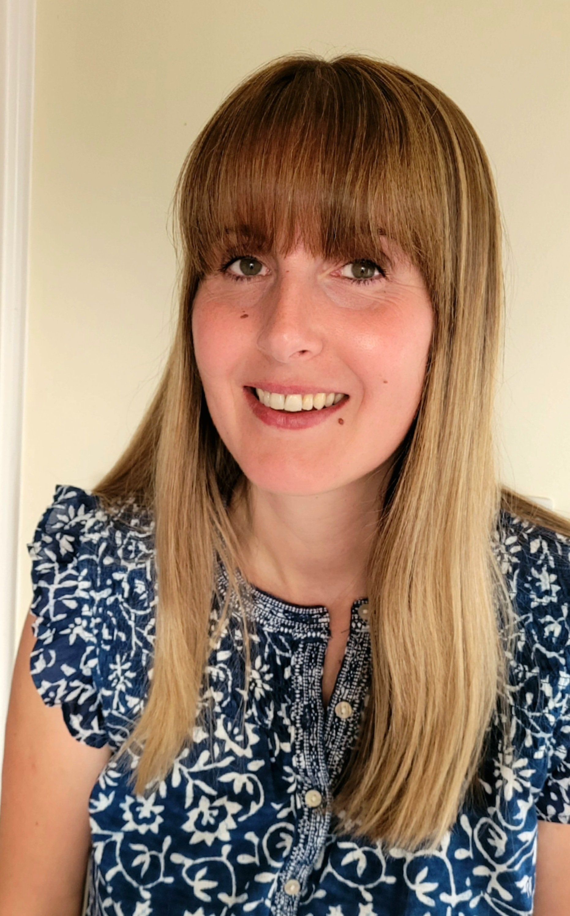 A woman wearing a blue and white floral shirt is smiling for the camera.