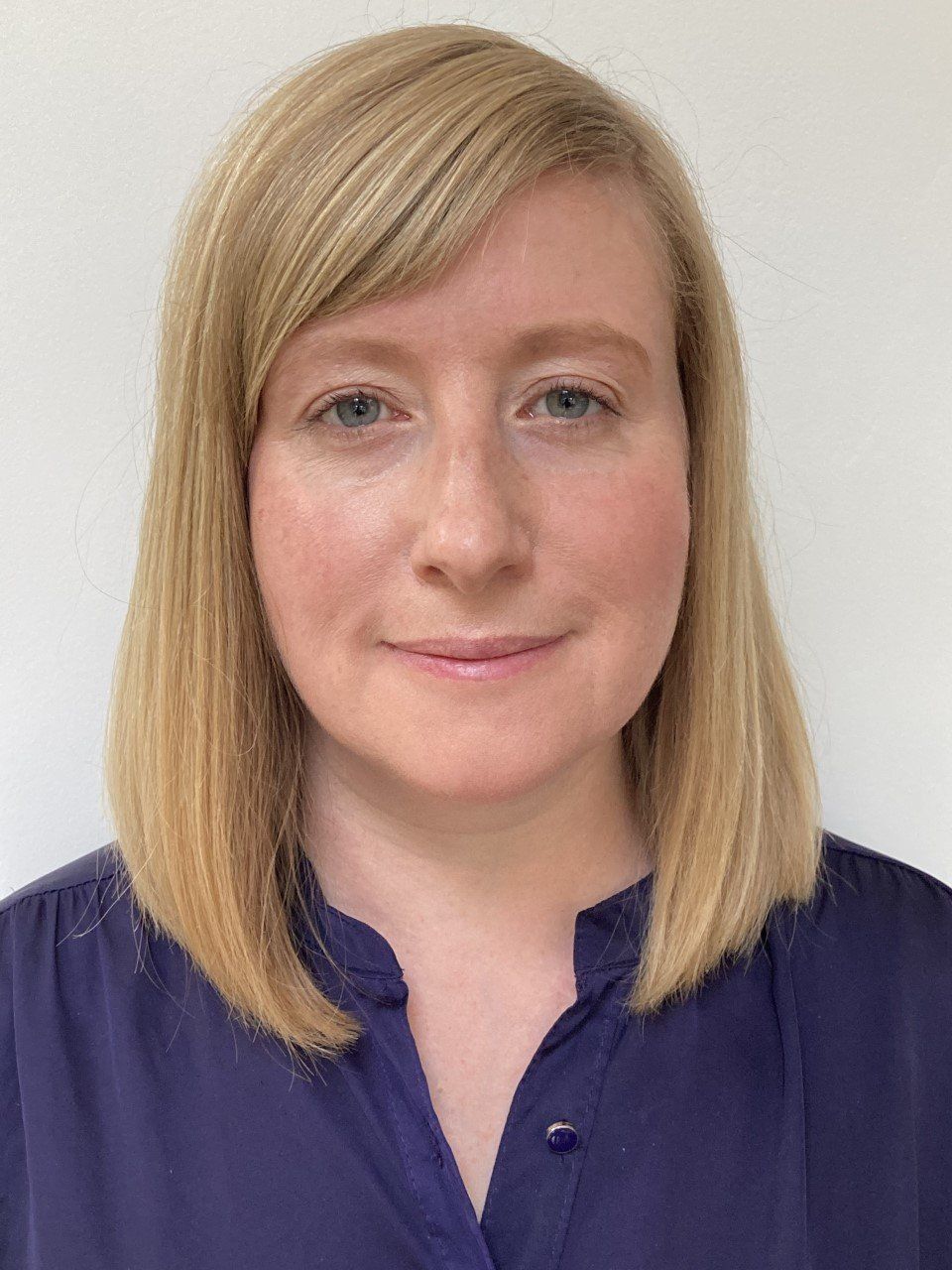 A woman with blonde hair is wearing a purple shirt and smiling for the camera.
