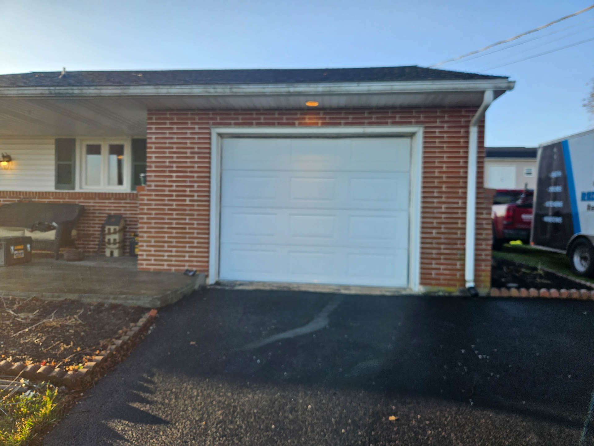 Brick garage with white door, black driveway, and a partial delivery truck at right.
