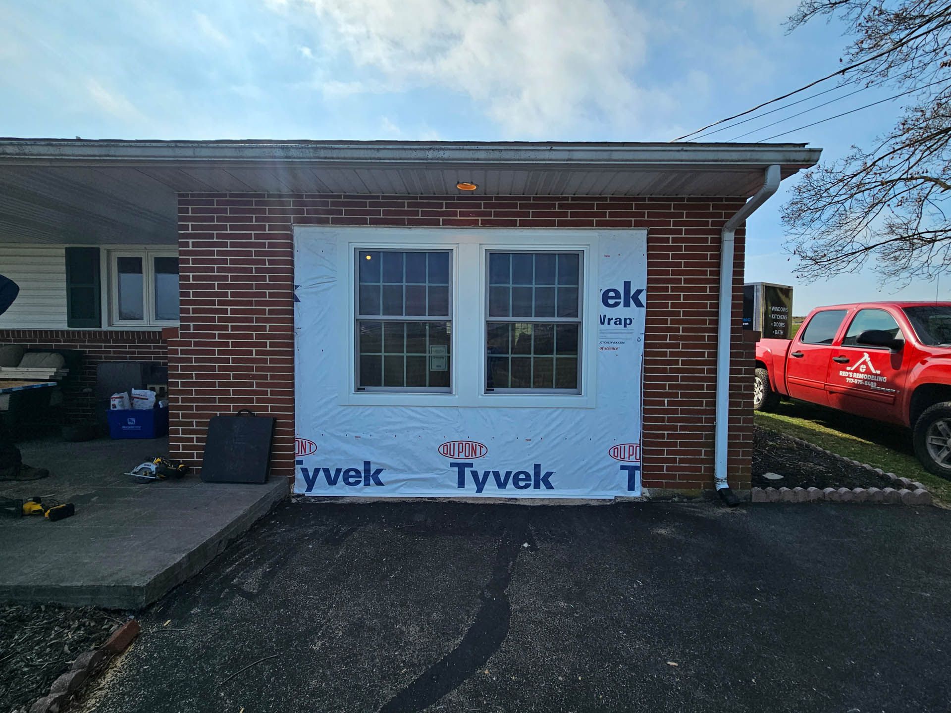 Small brick house addition under construction with Tyvek wrap and a red truck parked beside it.