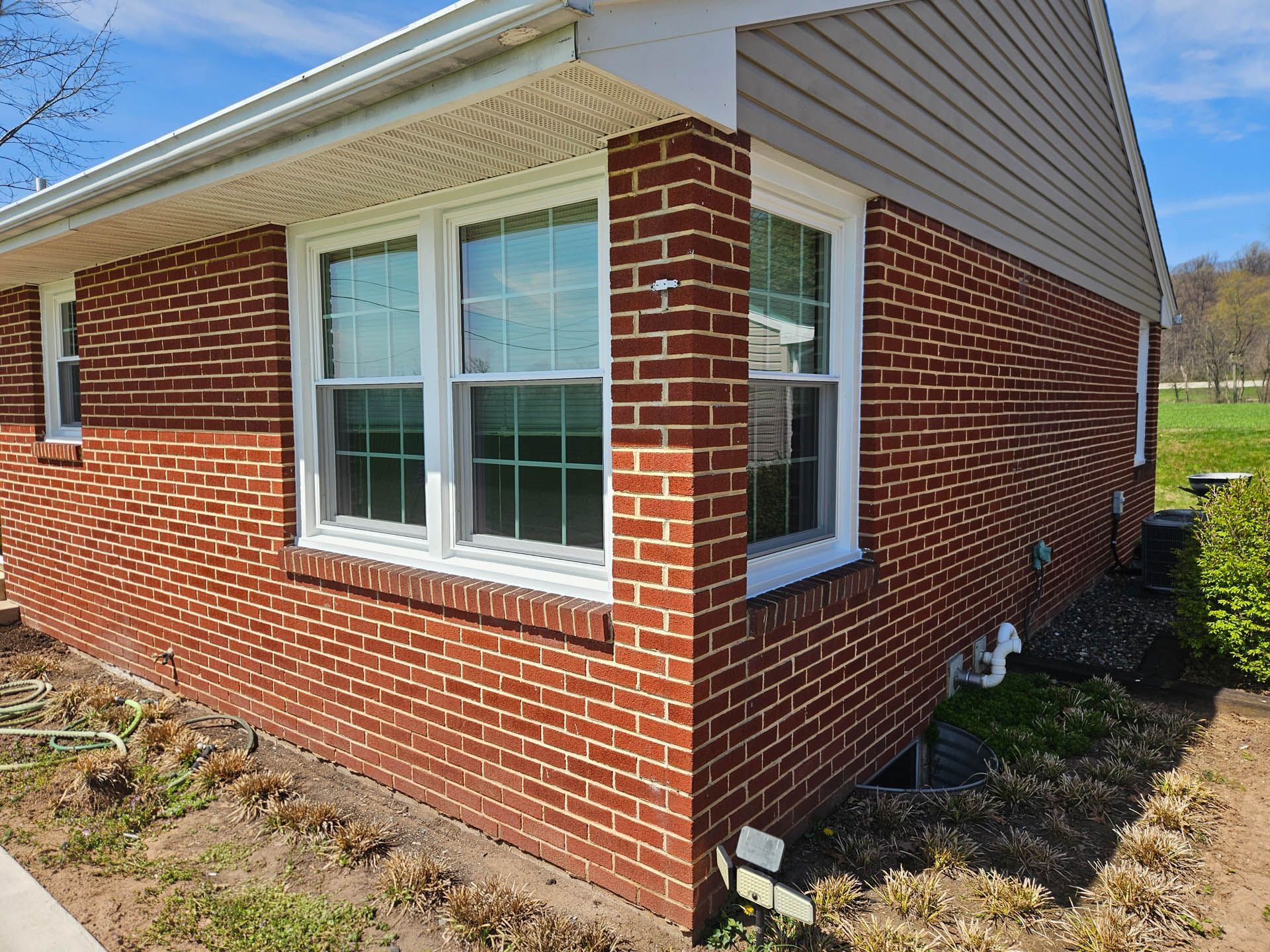 Side view of a brick house with white-trimmed windows and gray siding, beside a dirt yard
