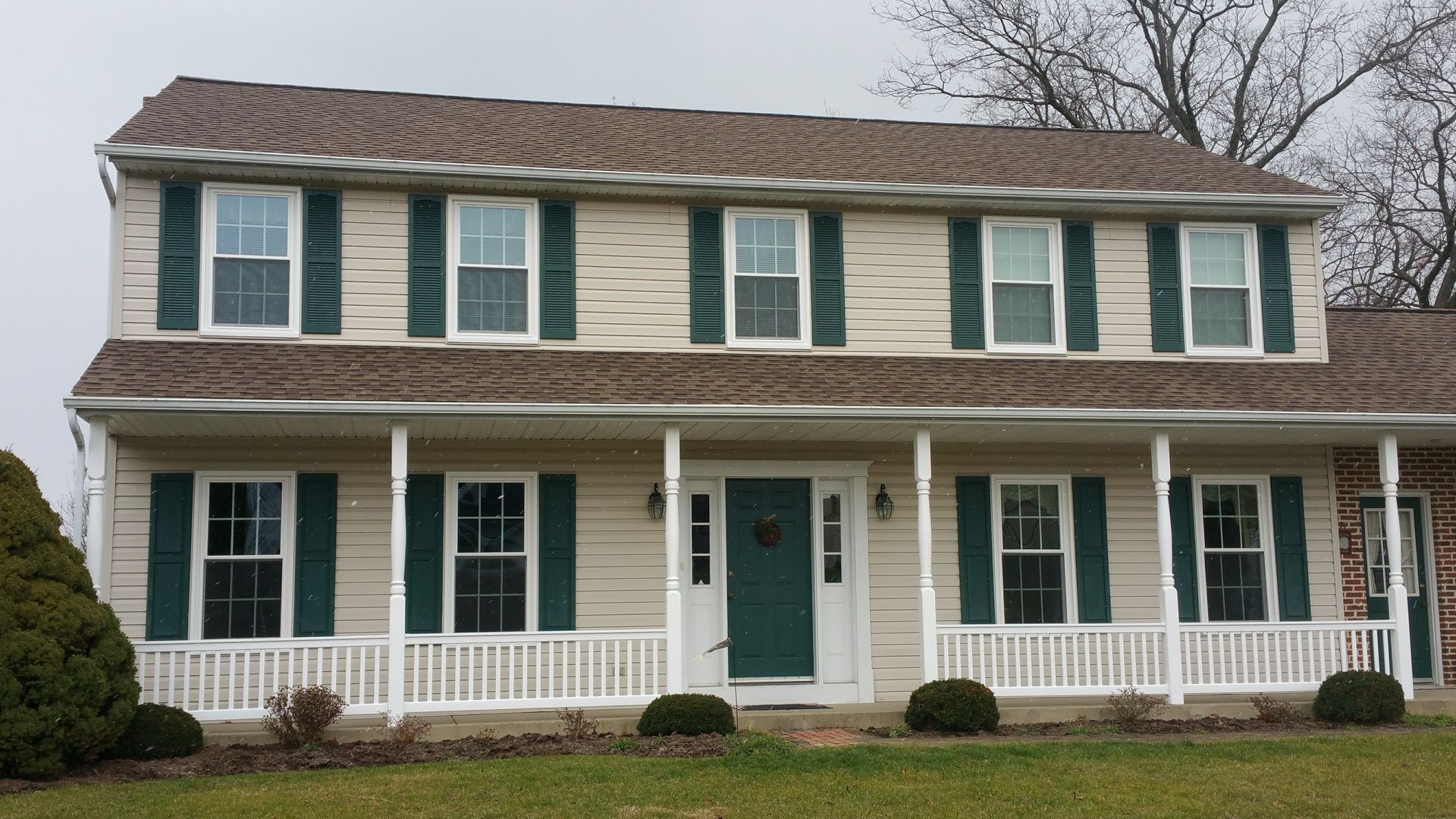 A two-story house with beige siding, a green front door and shutters, and a white porch with railings.