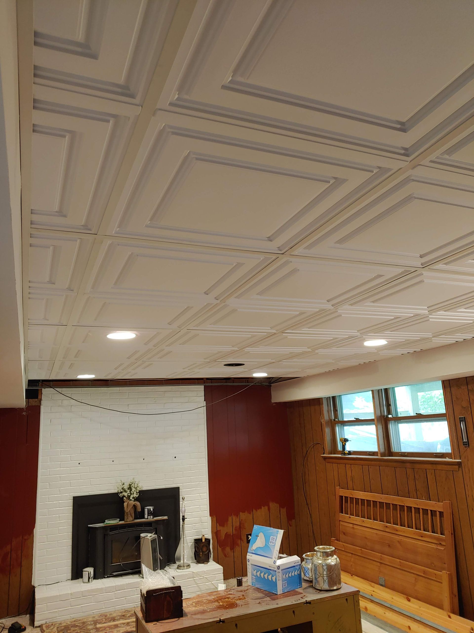 A room under renovation featuring a white coffered ceiling, a white-tiled fireplace, and walls partially painted dark red.