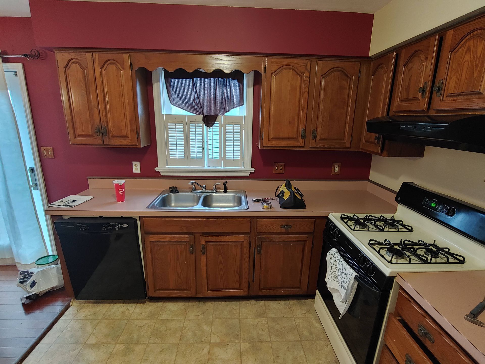 A kitchen with dark red walls, oak cabinets, light countertops, a sink, dishwasher, and a white stove.