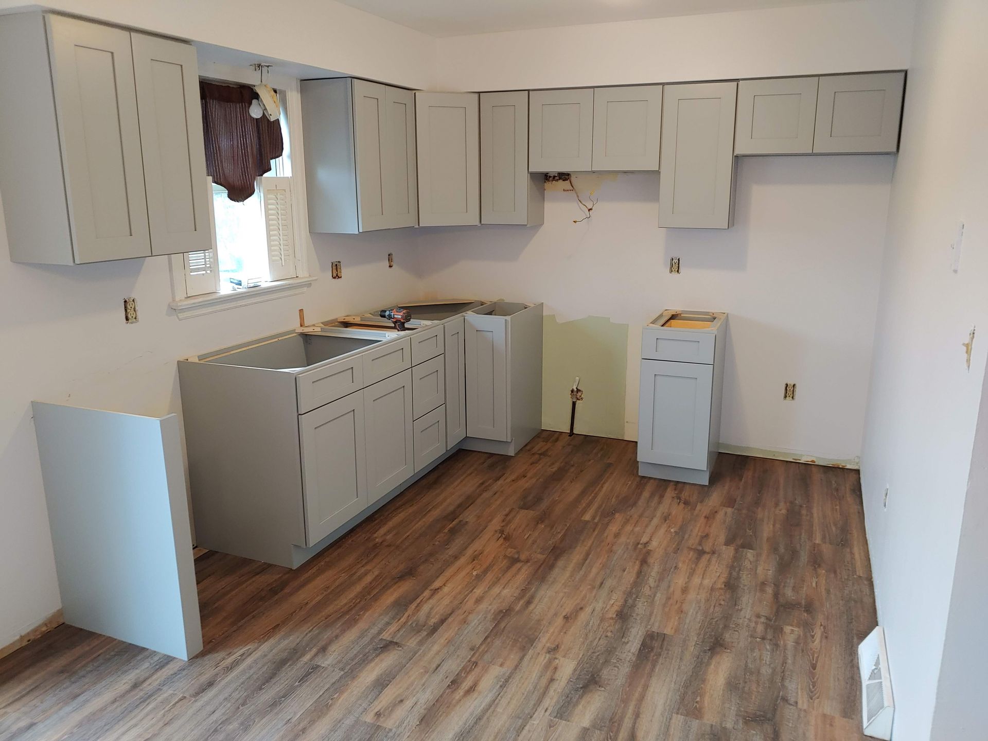 A kitchen under renovation with light gray cabinets, unfinished counters, and new wood-look flooring.