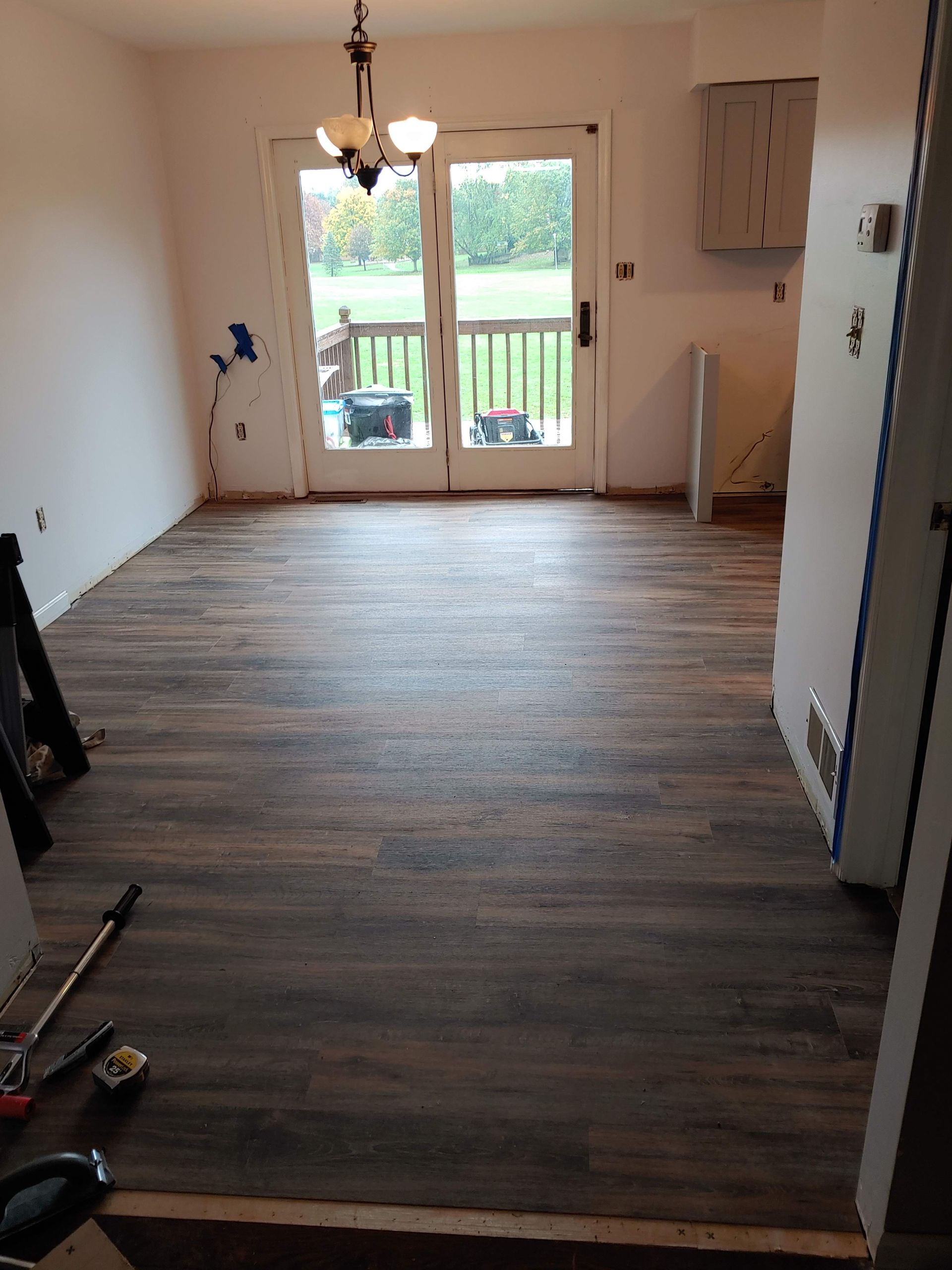 A room with dark wood-look plank flooring, light-colored walls, a chandelier, and double glass doors leading to a deck.