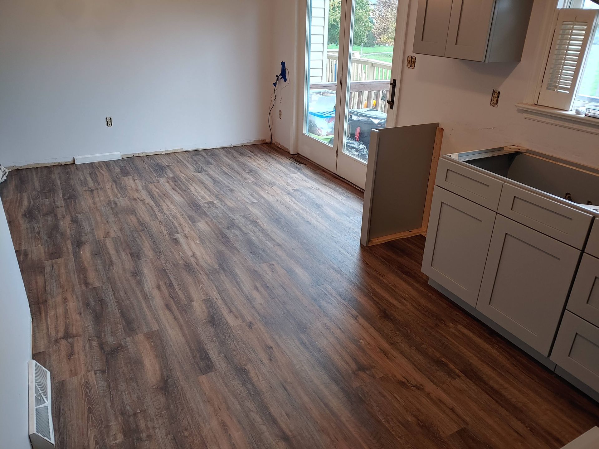 New wood-look laminate flooring installed in a kitchen space with gray cabinets, leading to a glass patio door.