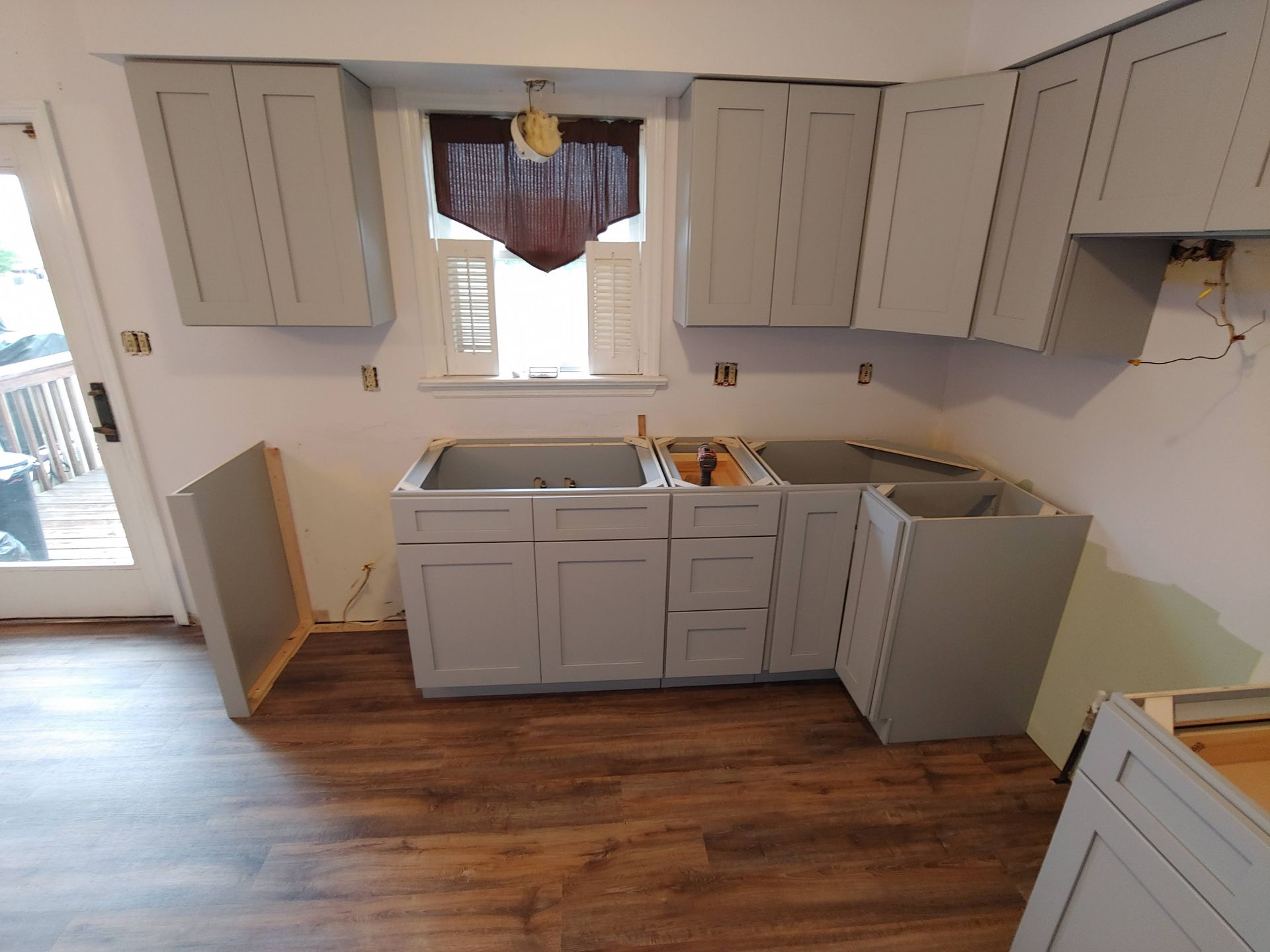 A kitchen undergoing renovation with light gray shaker-style cabinets installed against light-colored walls and wood floors.