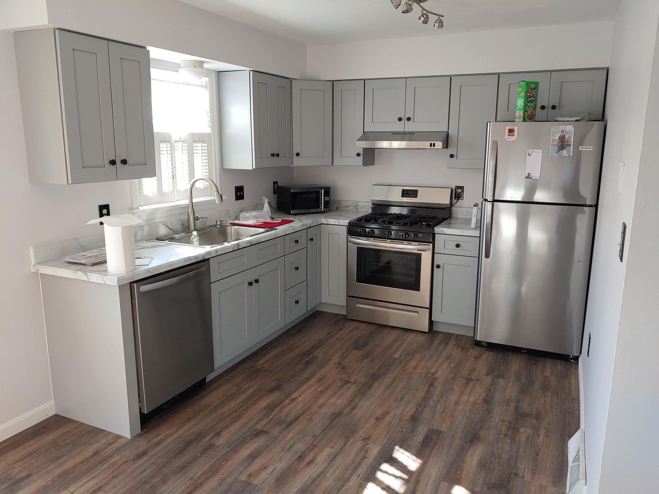 A kitchen with gray cabinets, stainless steel appliances, a light-colored countertop, and dark wood-look flooring.