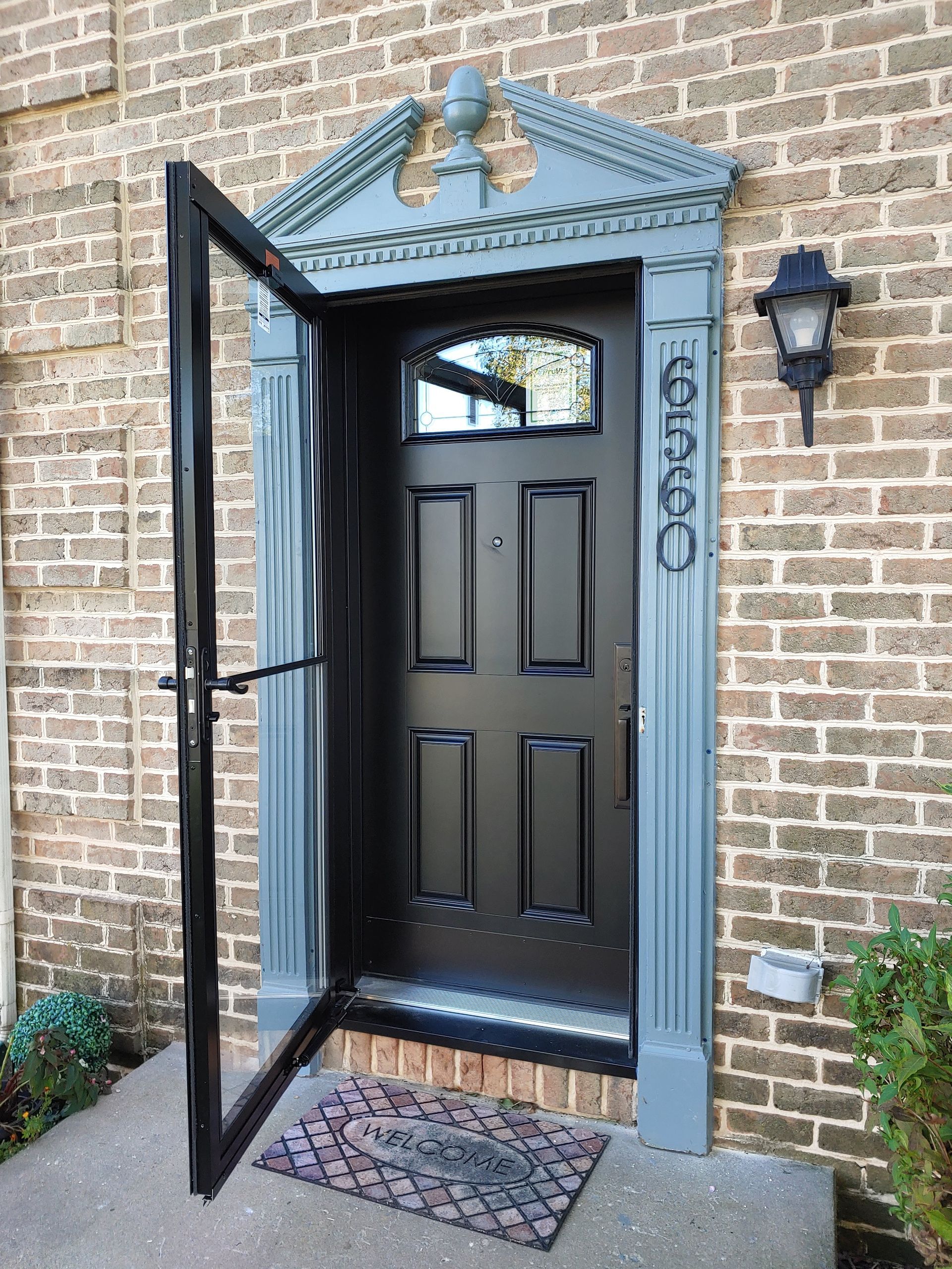 A black front door with a window set in a blue-grey architectural frame with a pediment, set against a tan brick wall.