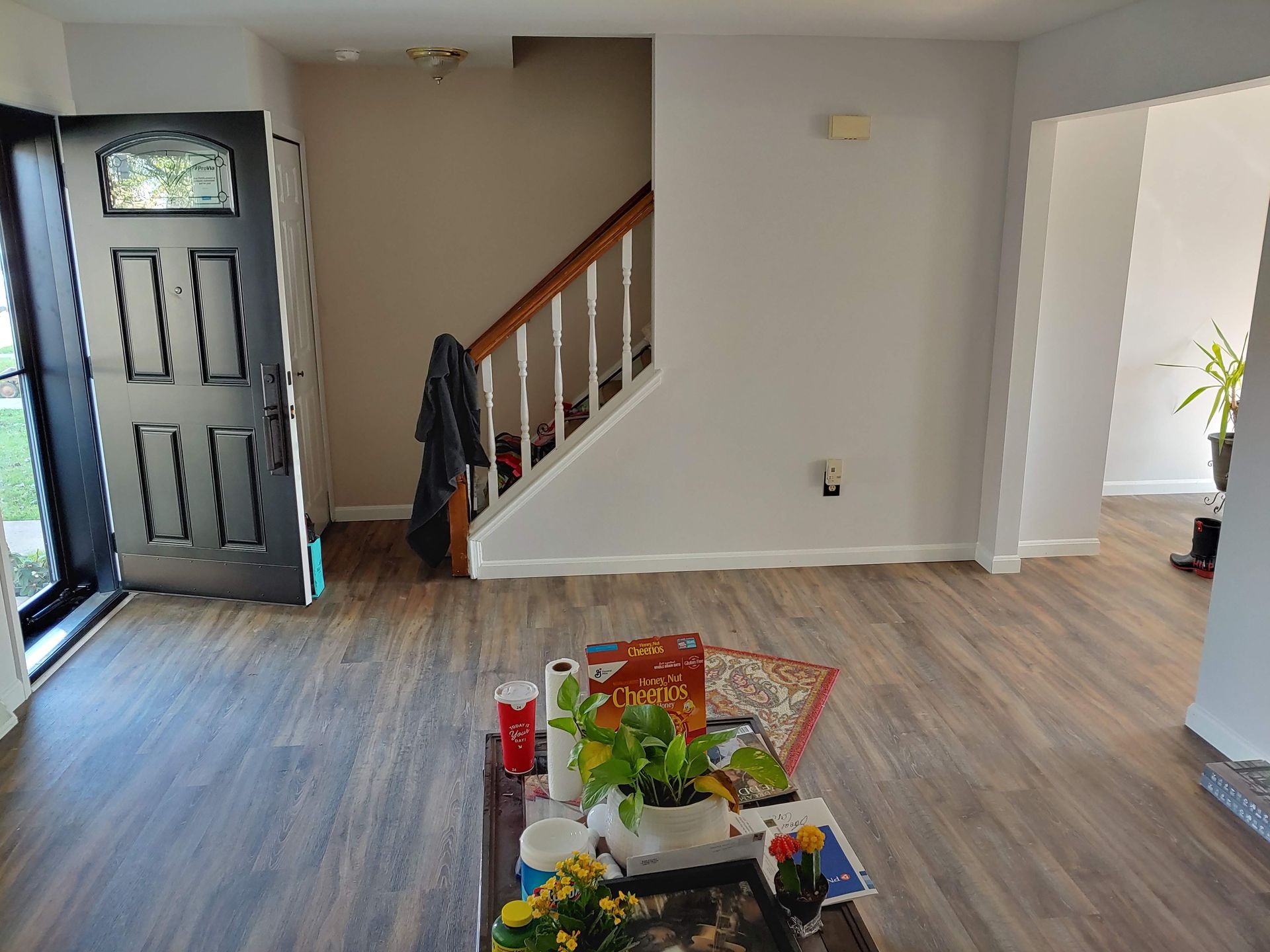 An entryway with a gray front door, a staircase with white railings, and wood-look flooring leading to another room.