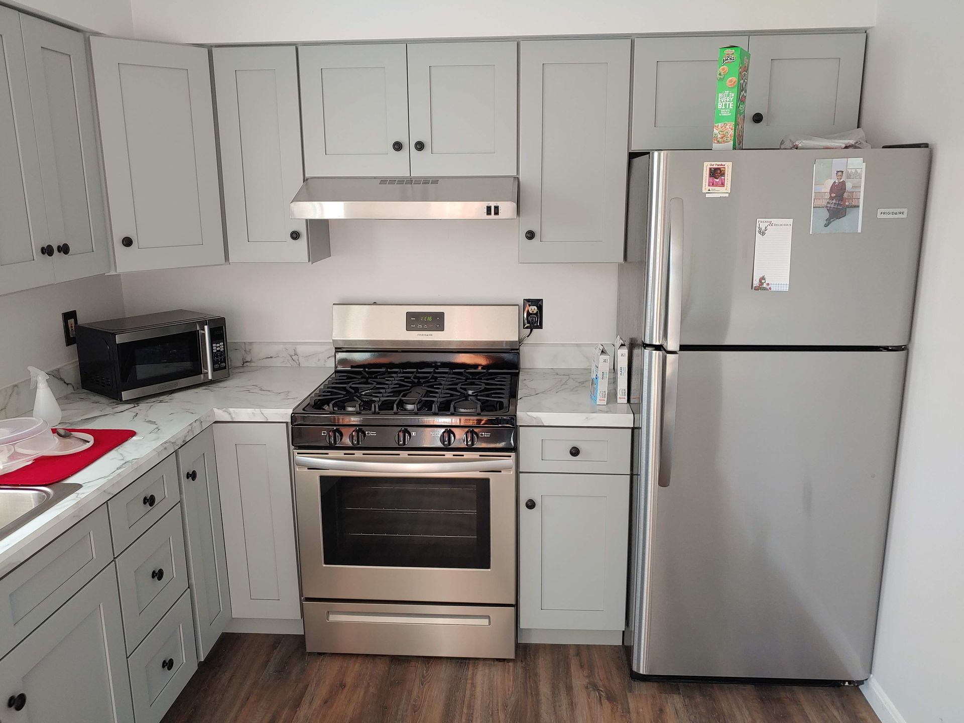 A kitchen featuring gray cabinets, a stainless steel gas range with a vent hood, and a stainless steel refrigerator.