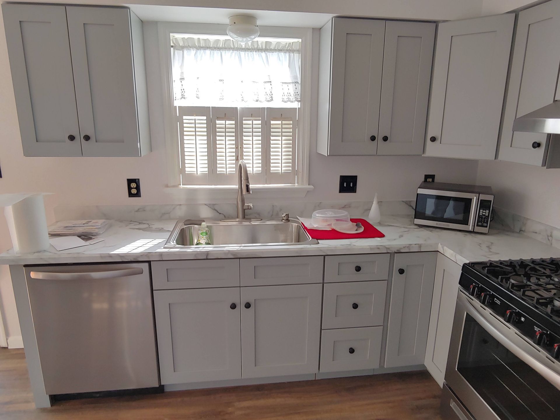 A kitchen with light gray cabinets, white marble-patterned countertops, a stainless steel sink, and a stainless oven.