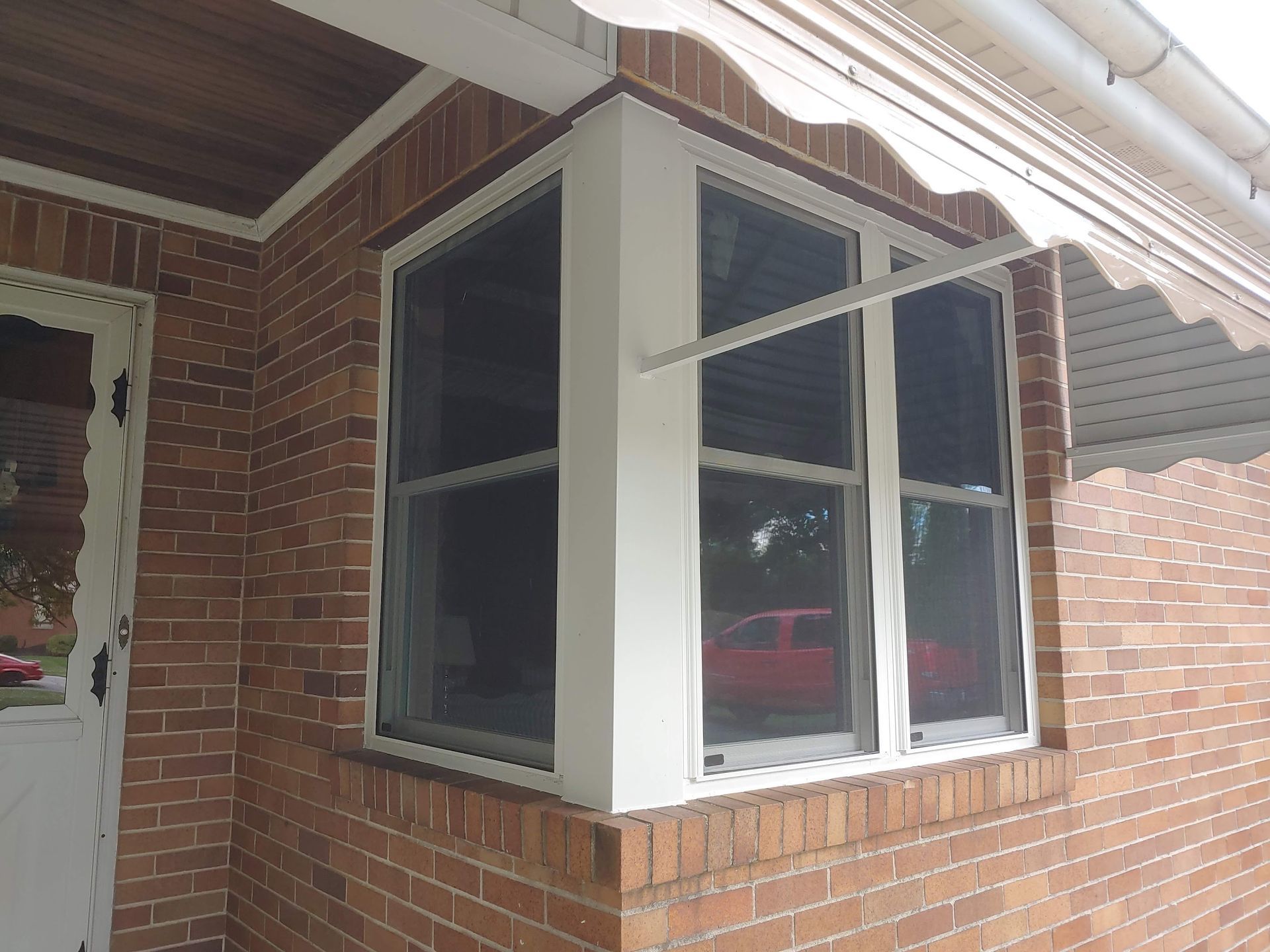 A brick home corner with a white-trimmed bay window and a white metal awning above.