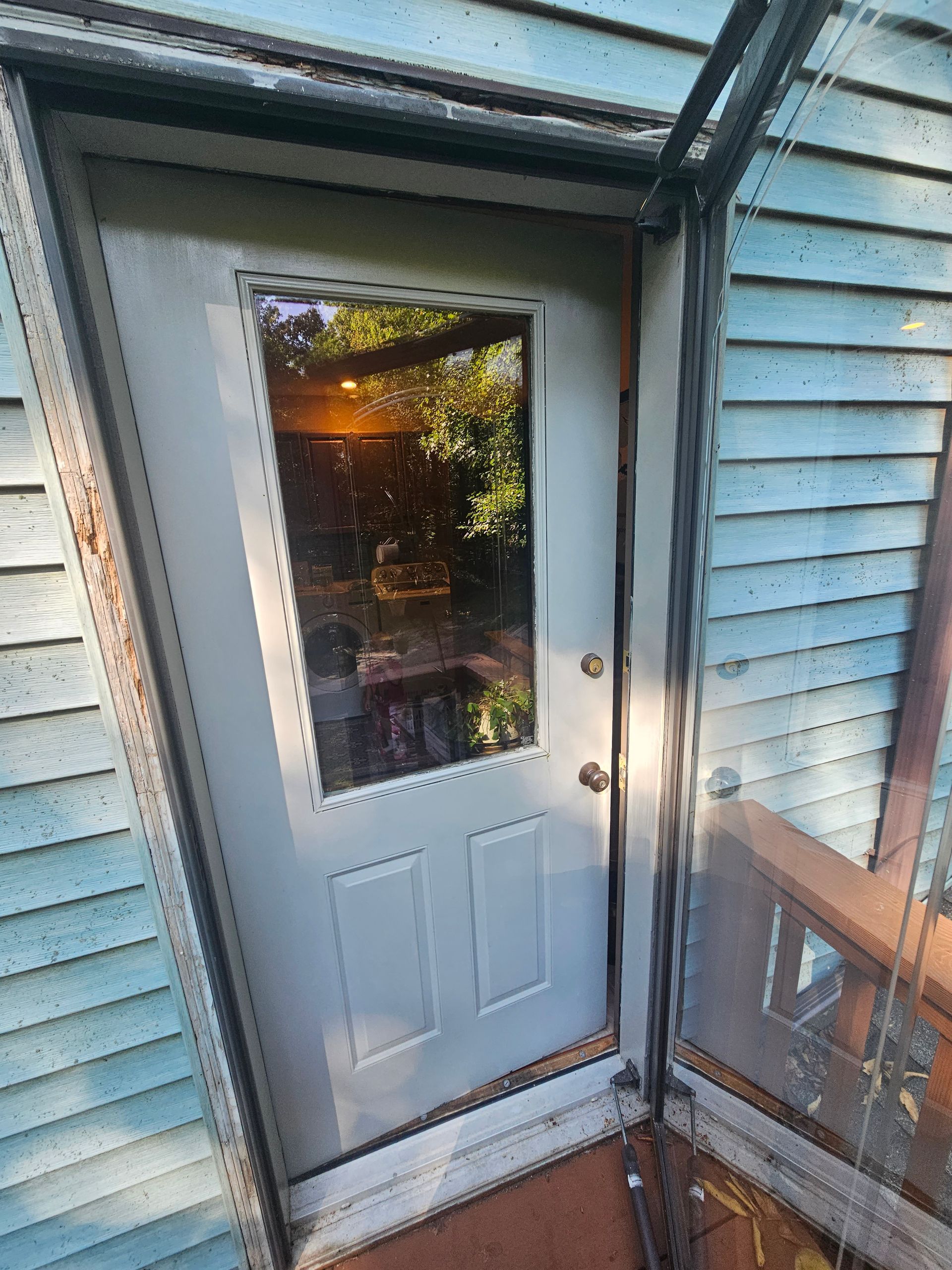 A grey exterior door with a glass window panel on the upper half, set within light blue horizontal siding.