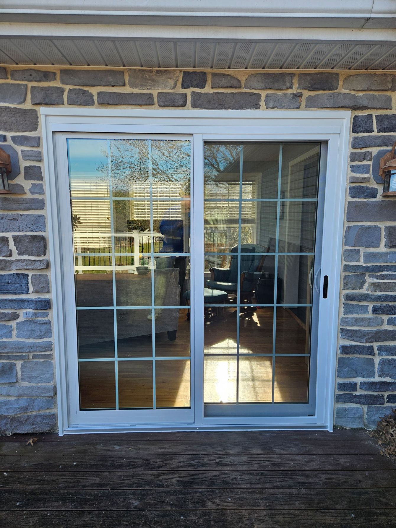 A white sliding glass door with a grid pattern, installed in a stone exterior wall leading to a sunlit indoor room.