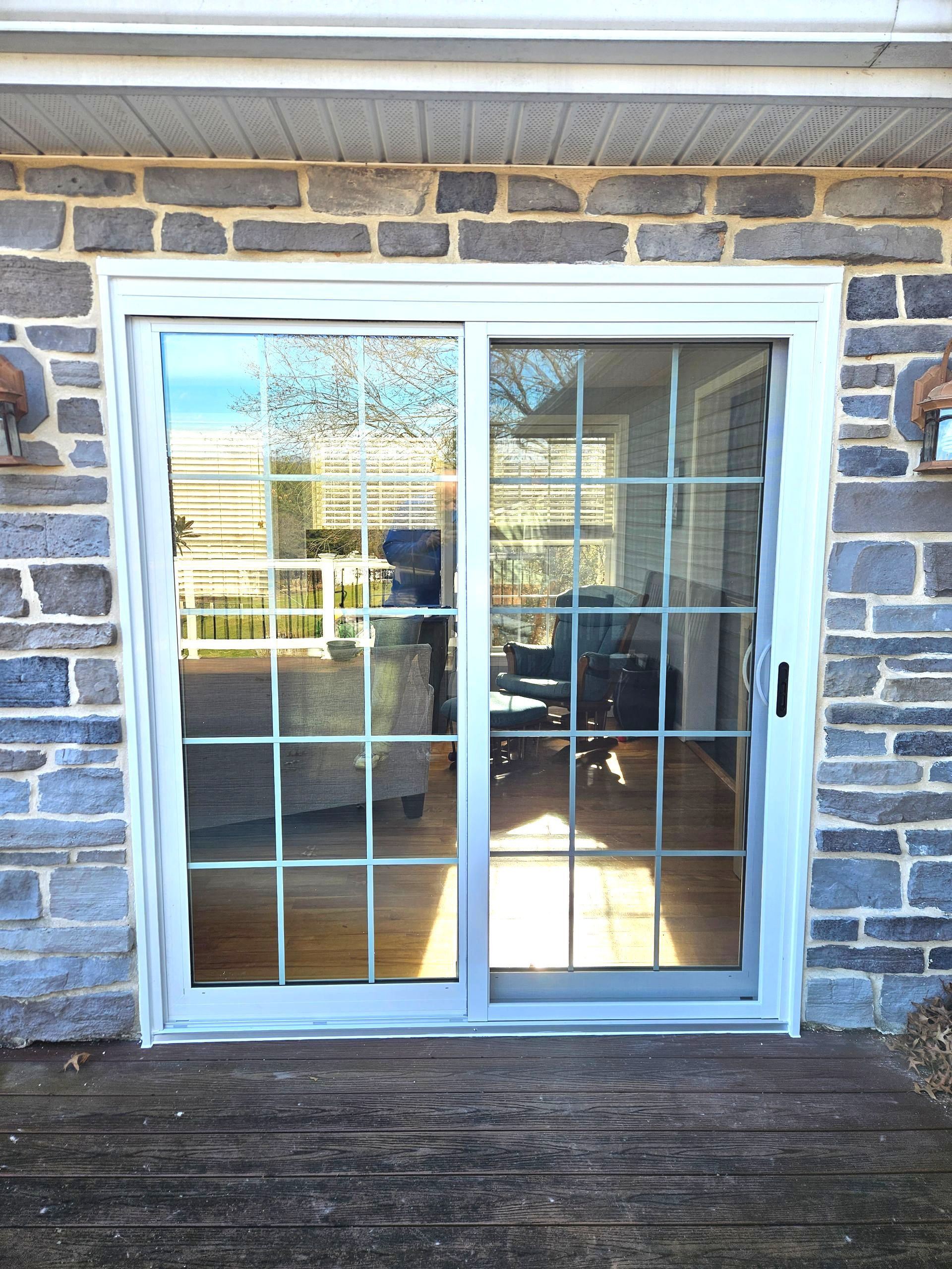 A sliding glass patio door with a white frame and a grid pattern, set into an exterior stone wall above a wooden deck.
