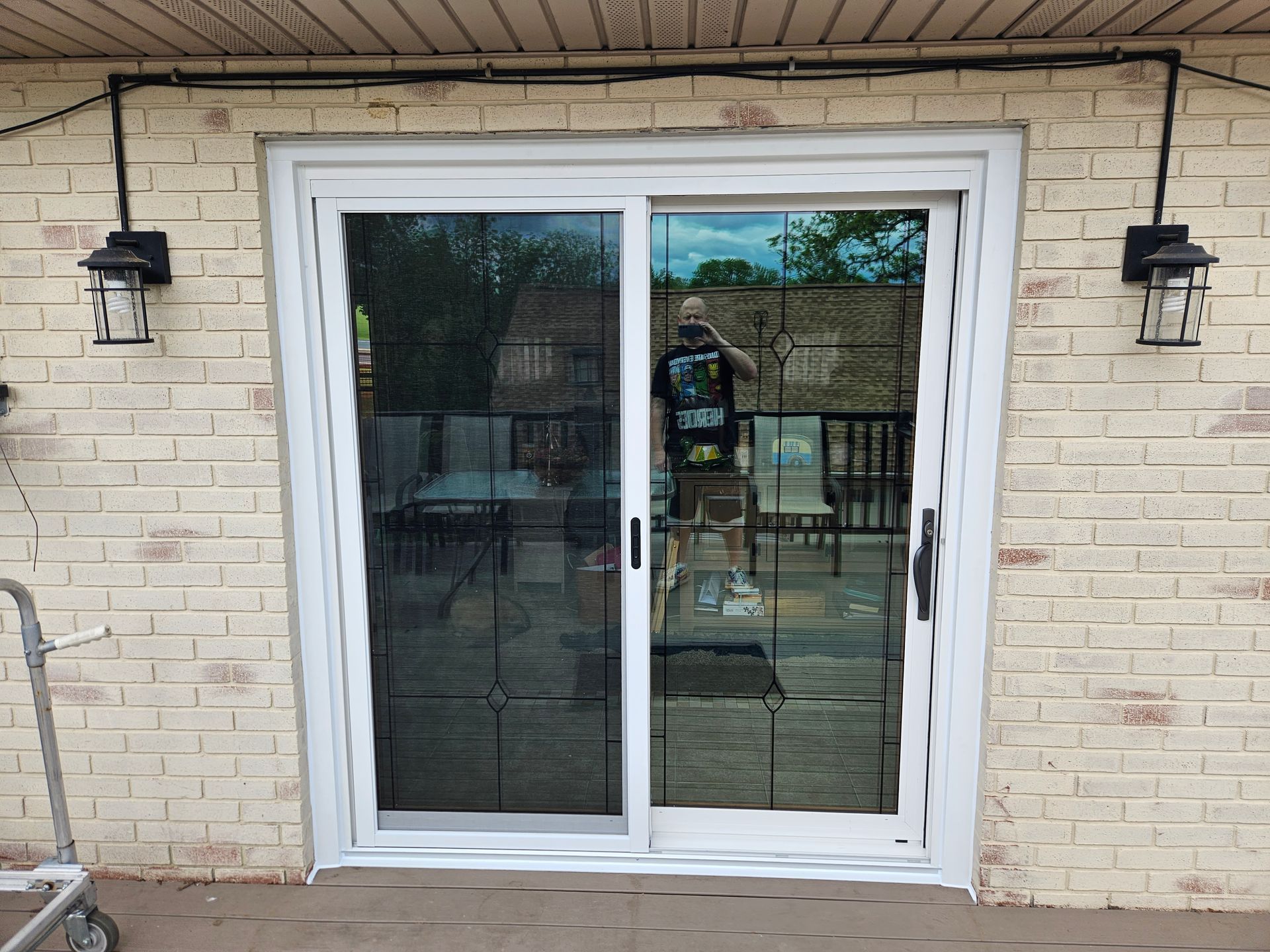White sliding glass patio door on a light brick wall, flanked by two black outdoor wall lanterns.