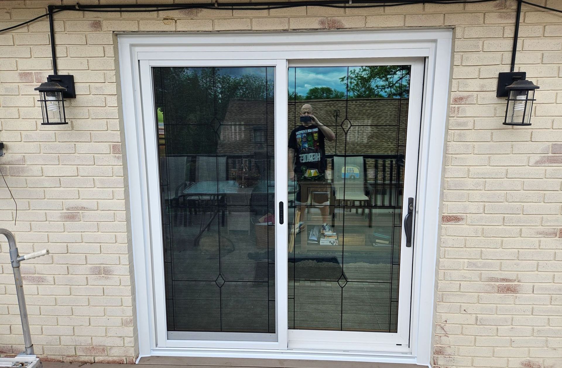 A white-framed sliding glass door on a light brick wall, flanked by two outdoor wall lamps.
