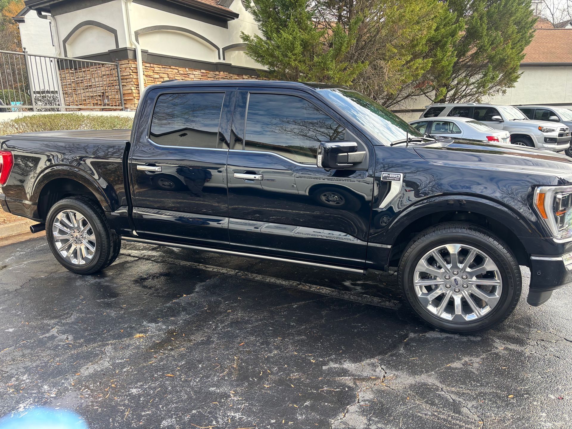 Black Ford pickup truck parked on wet pavement near a building and other vehicles.