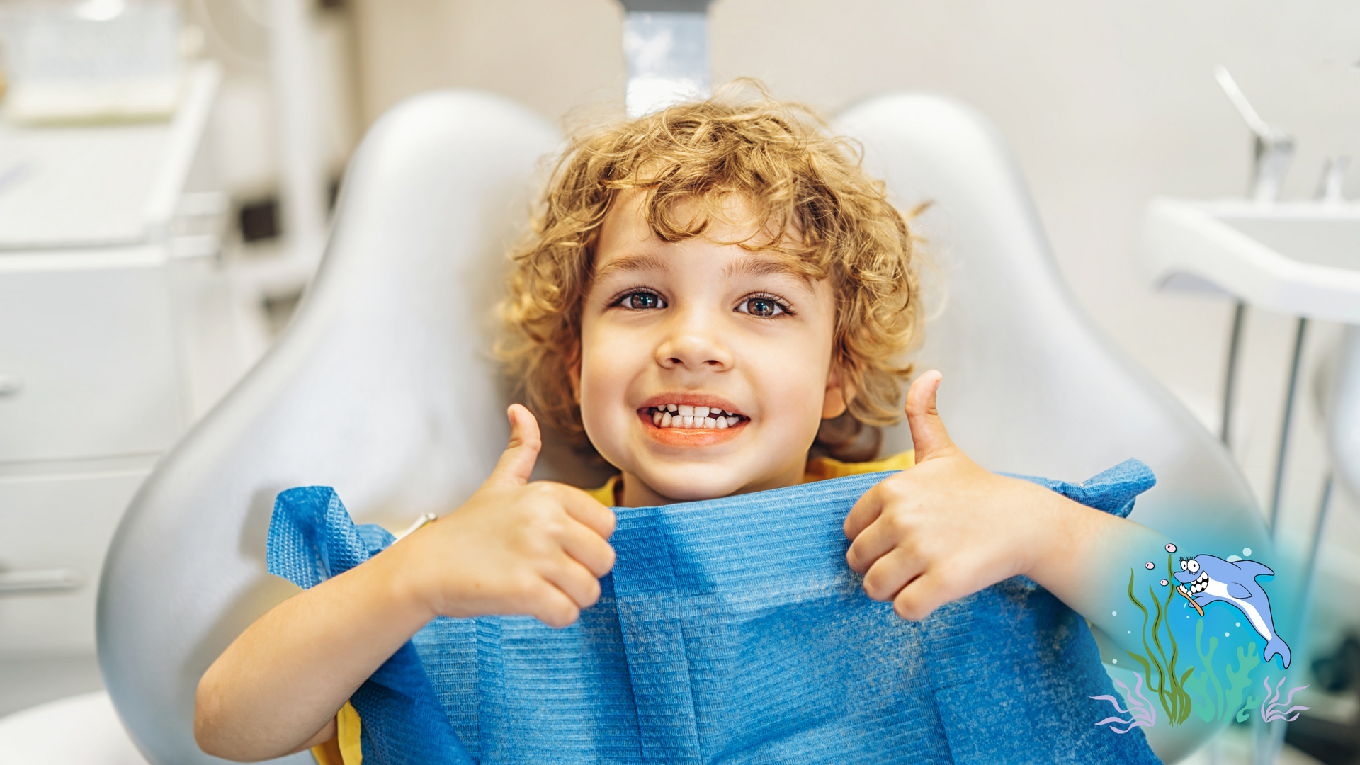 Boy in dentist chair, thumbs up. Curly hair, blue bib, bright smile. Dentist office setting.