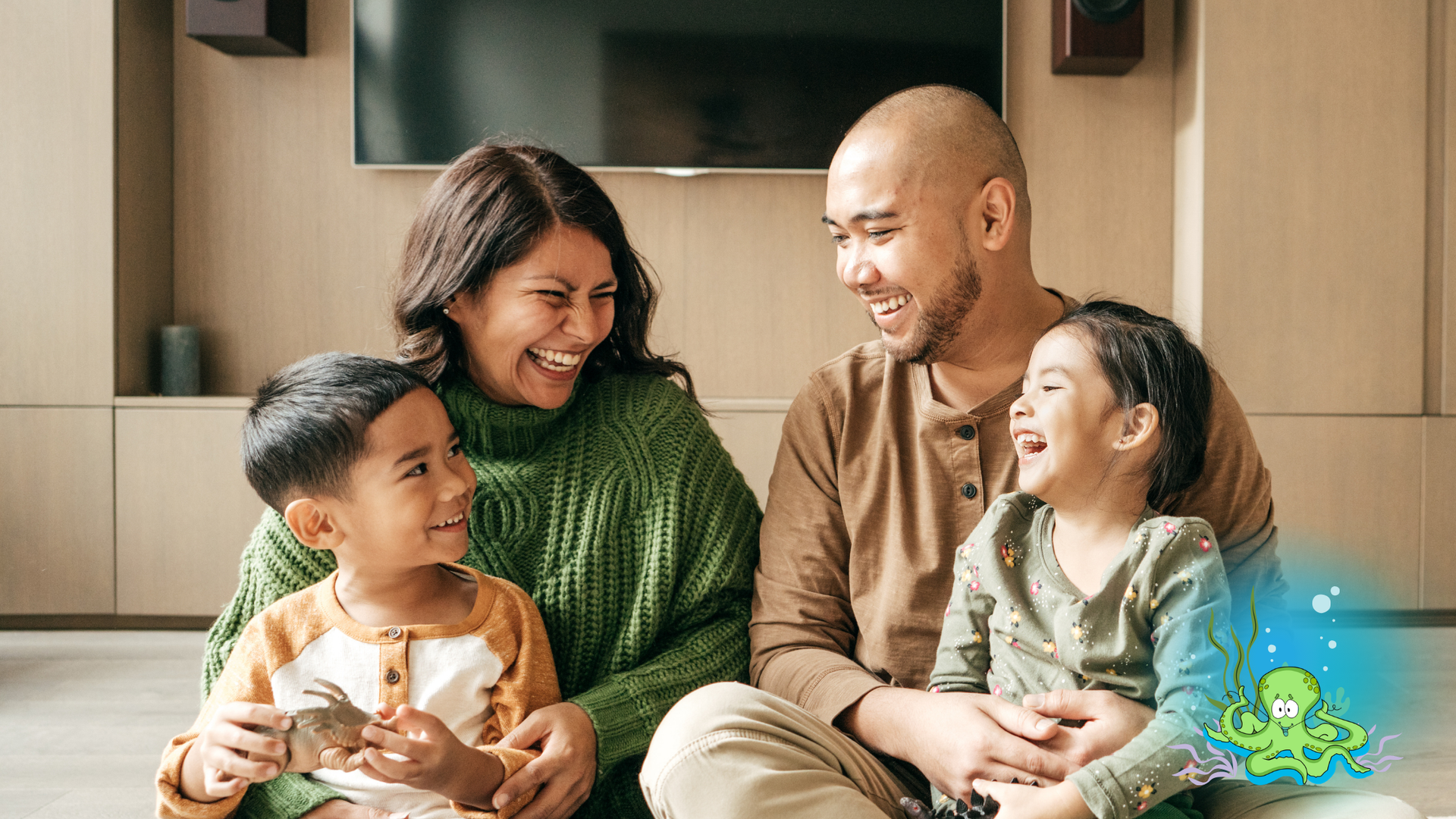 A smiling family sits together indoors in a living room, laughing and interacting happily.