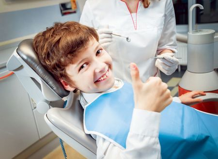 A young boy is giving a thumbs up while sitting in a dental chair.