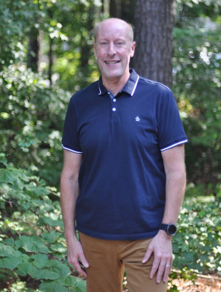 A man in a blue polo shirt is standing in the woods.