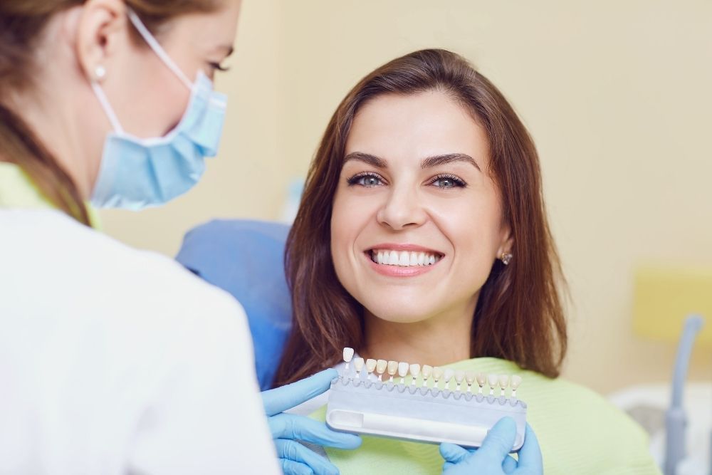 Woman smiles while dentist holds shade guide in a dental office.