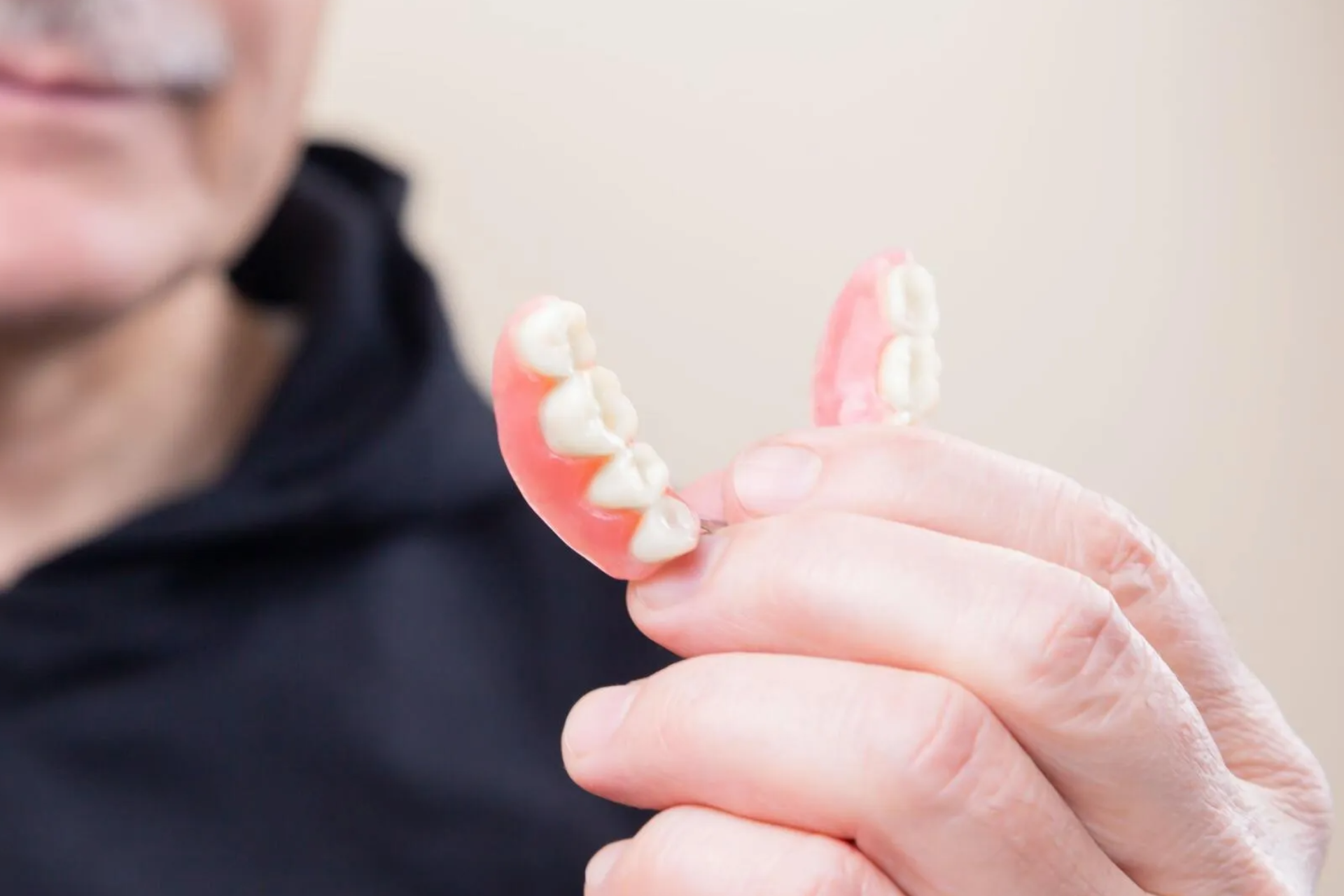 Person holding a set of dentures, pink and white, in front of their face.