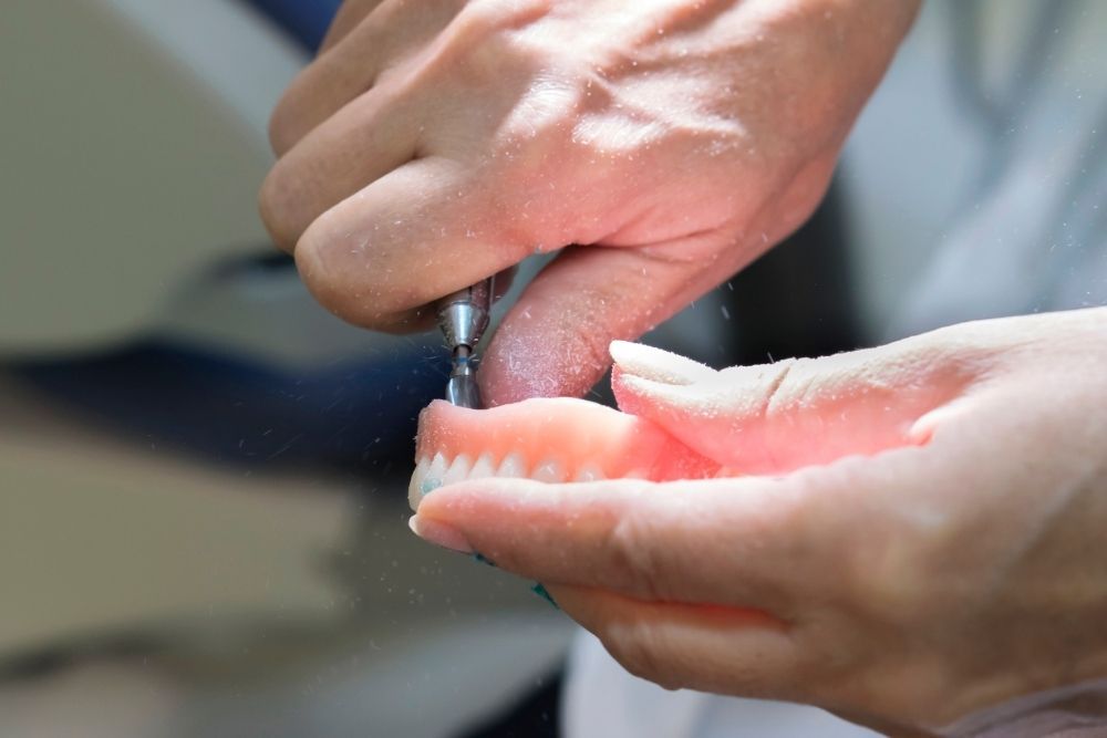 Hands holding and using a tool to work on a set of dentures.