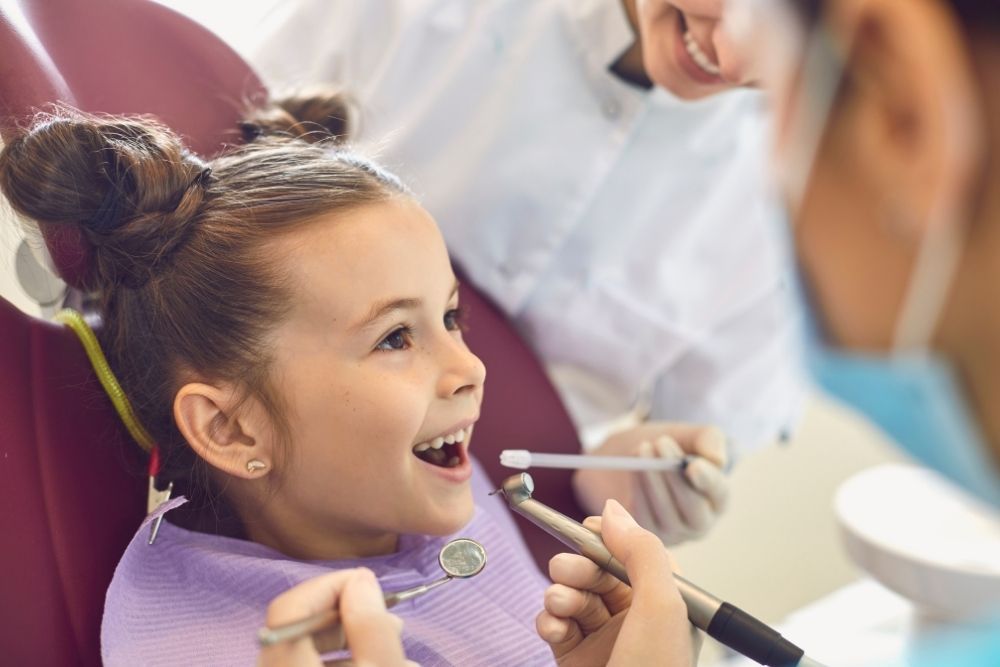 Young child at dentist with mouth open; dentist holding tools.