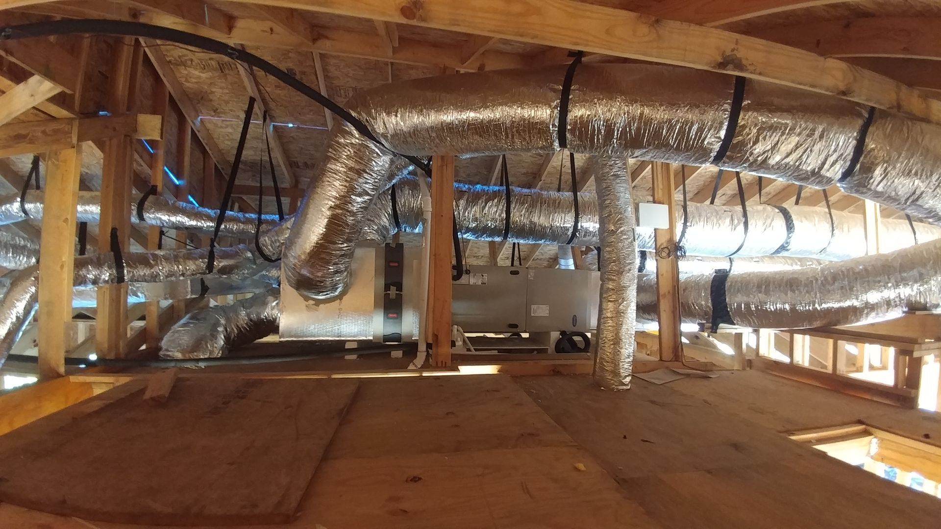 Attic interior with exposed ductwork, wooden beams, and insulation under the roof.