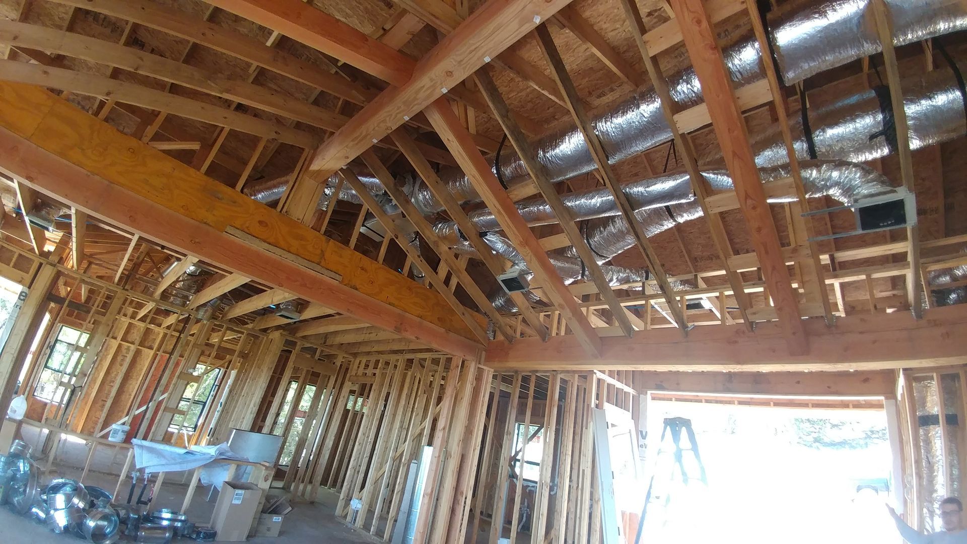 Unfinished wooden house interior with exposed roof trusses and bright daylight through open framing.