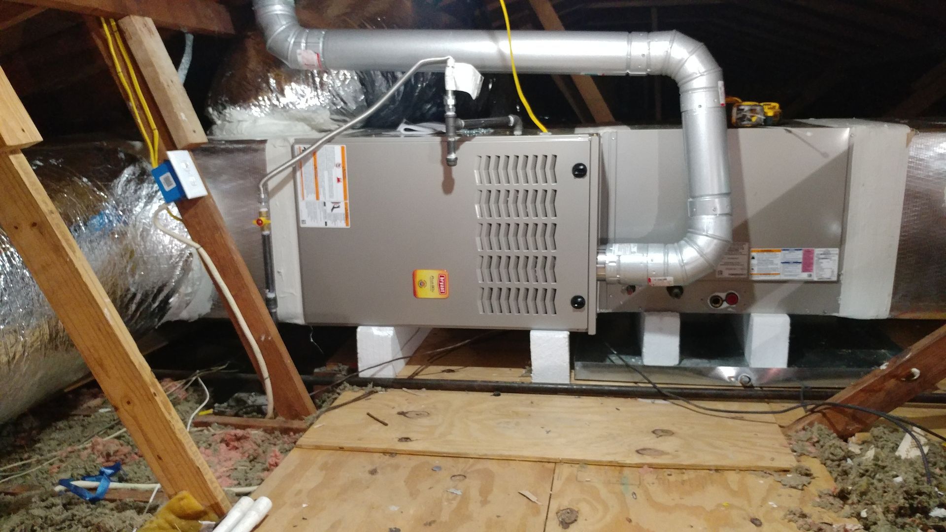 HVAC furnace and ductwork installed in an attic with exposed insulation and wooden framing