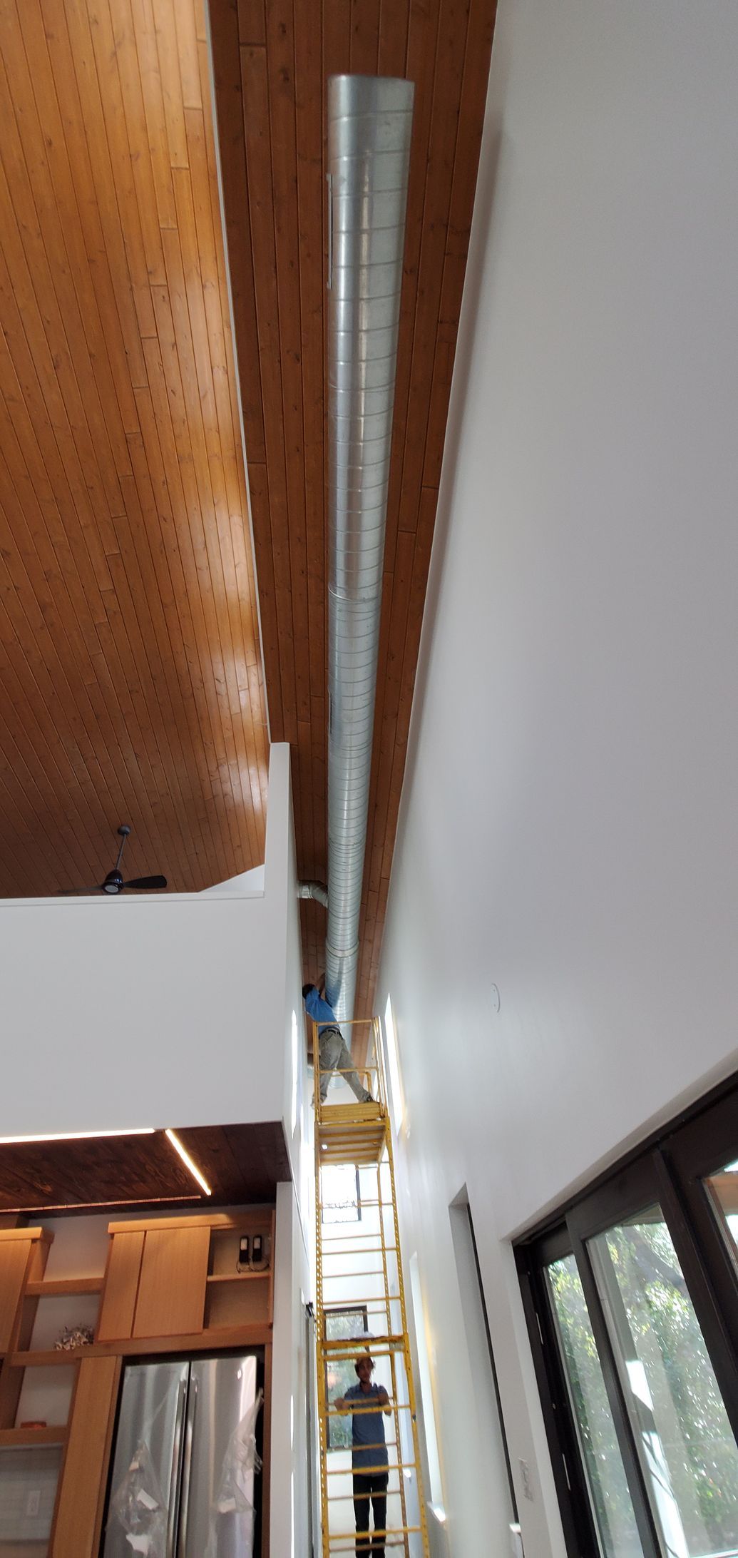 Narrow interior shaft with a ladder reaching up between a wood ceiling and white wall panels