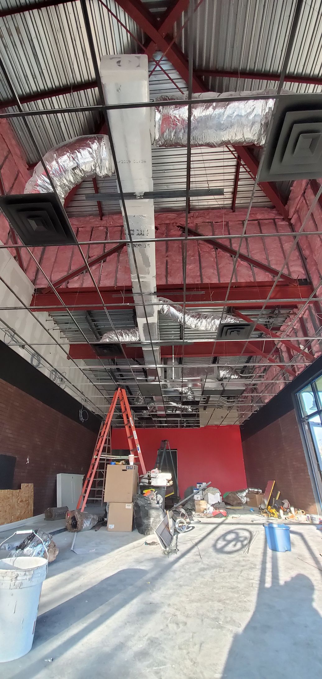 Interior of a building under renovation, with exposed red steel beams, ladders, and construction materials scattered on the floor.