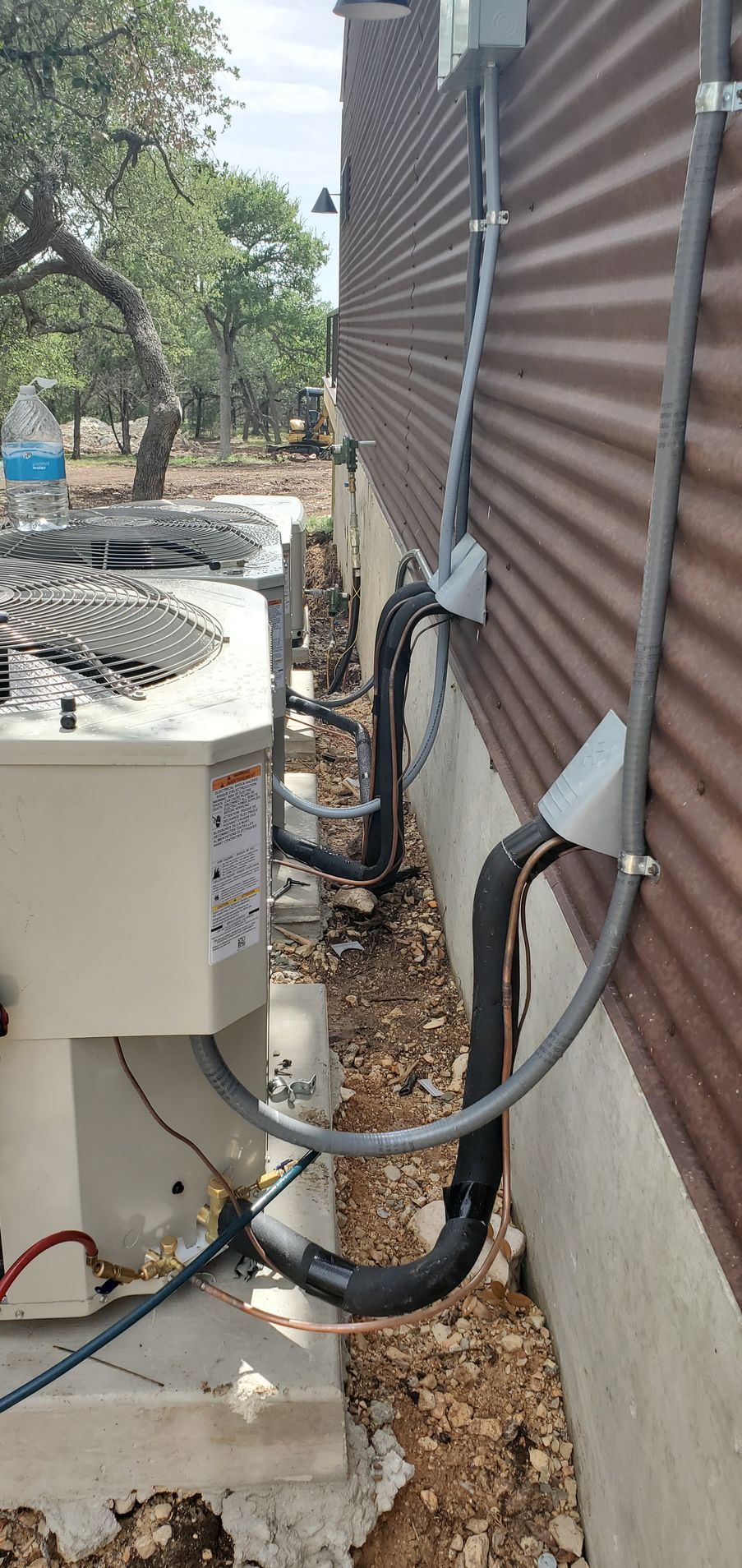 Outdoor HVAC equipment and conduit lines beside a brown wall on gravel ground