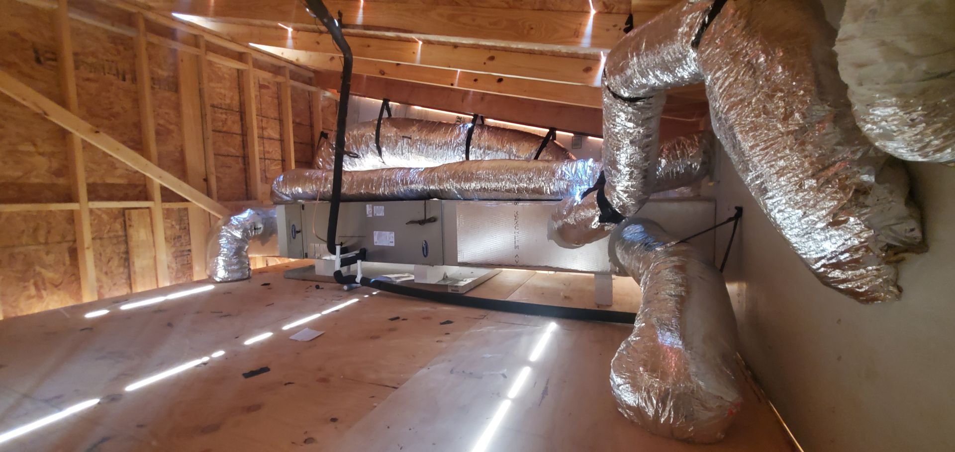 Unfinished attic with exposed wooden framing, insulation ducts, and sunlight on the floorboards