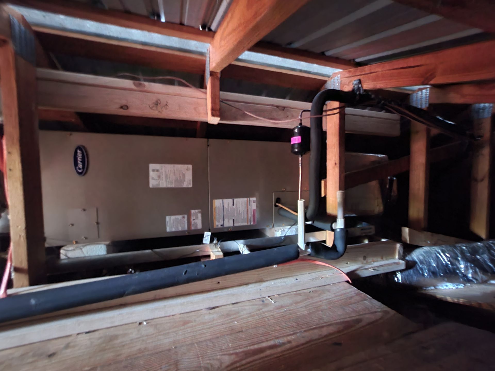 Wooden attic crawlspace with exposed beams, insulation, and ducting under a low roof