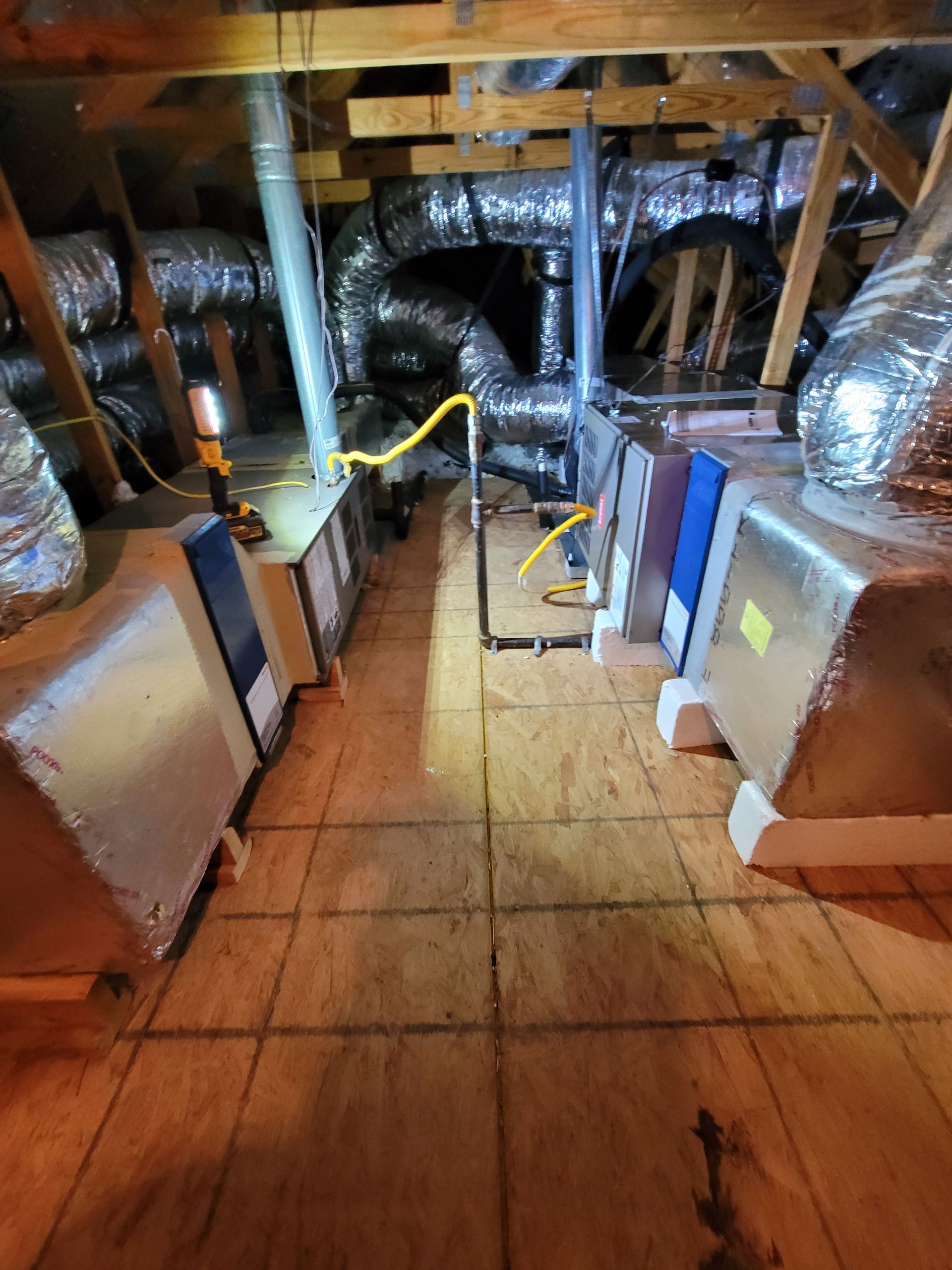 Attic crawlspace with exposed ducts, pipes, and HVAC units under wooden beams