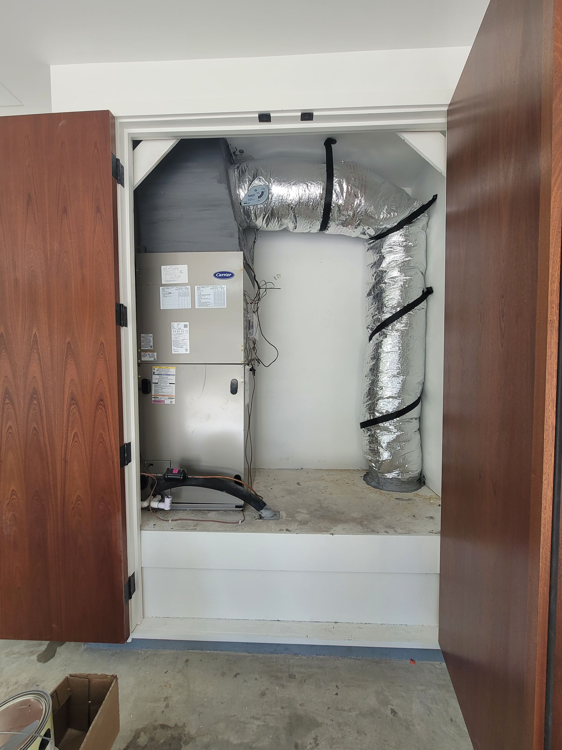 Open utility cabinet with exposed ductwork and damaged insulation between two wooden doors.