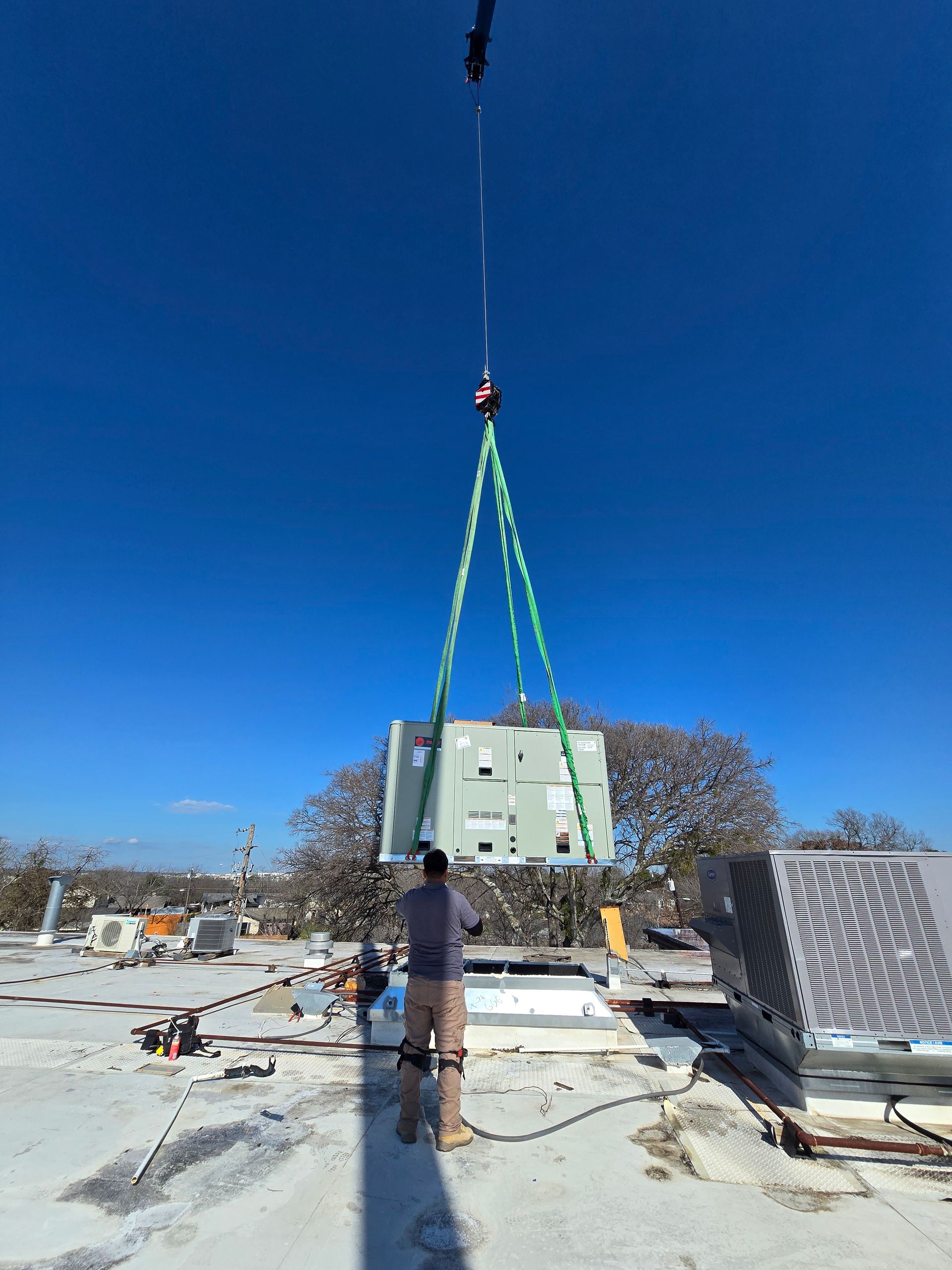 Crane lifting a white building module on green straps at a snowy construction site under a clear blue sky