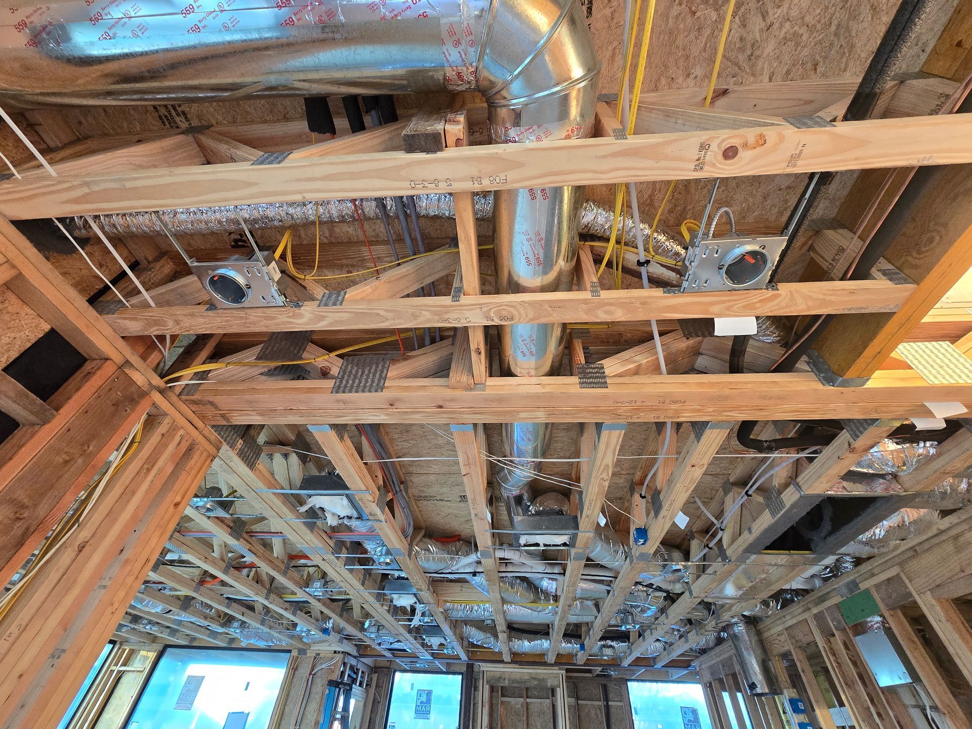 Exposed wooden ceiling framing with silver HVAC ducts and wiring in a house under construction