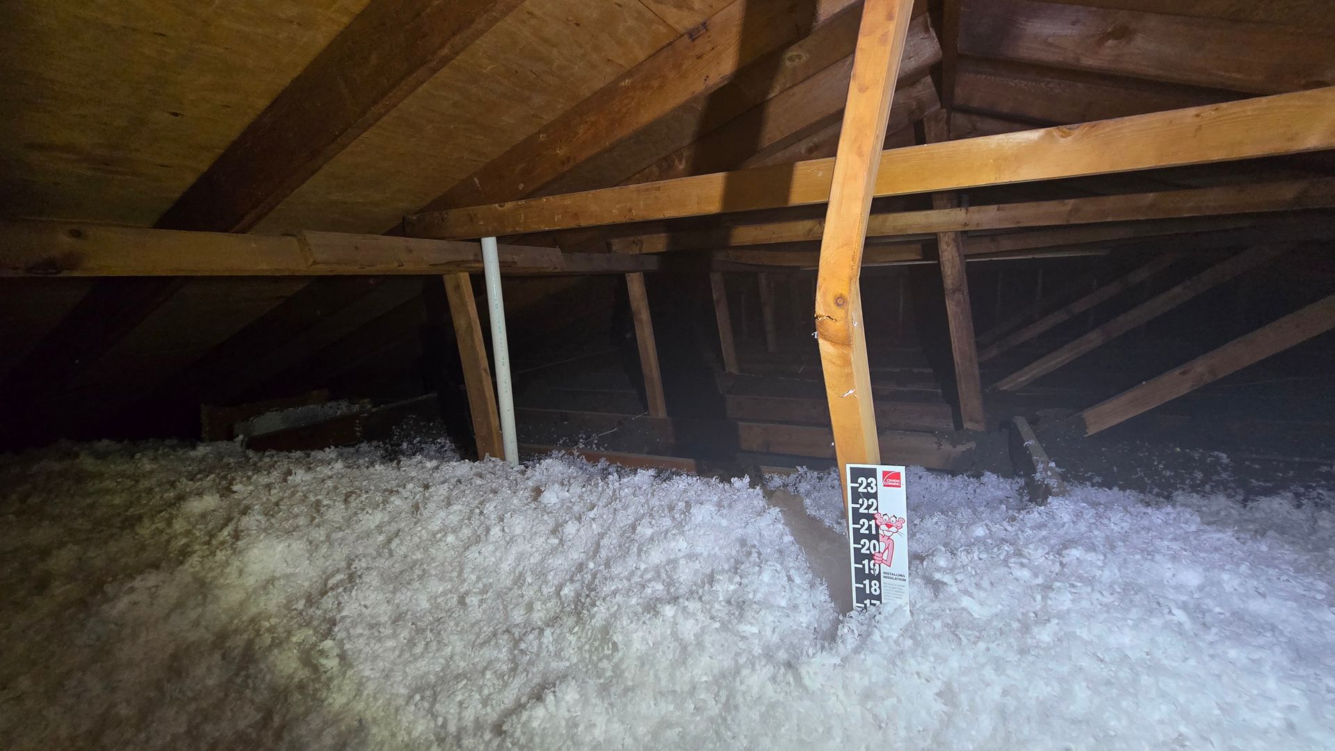 Attic with exposed wooden rafters and blown-in insulation; a vent pipe rises near center.