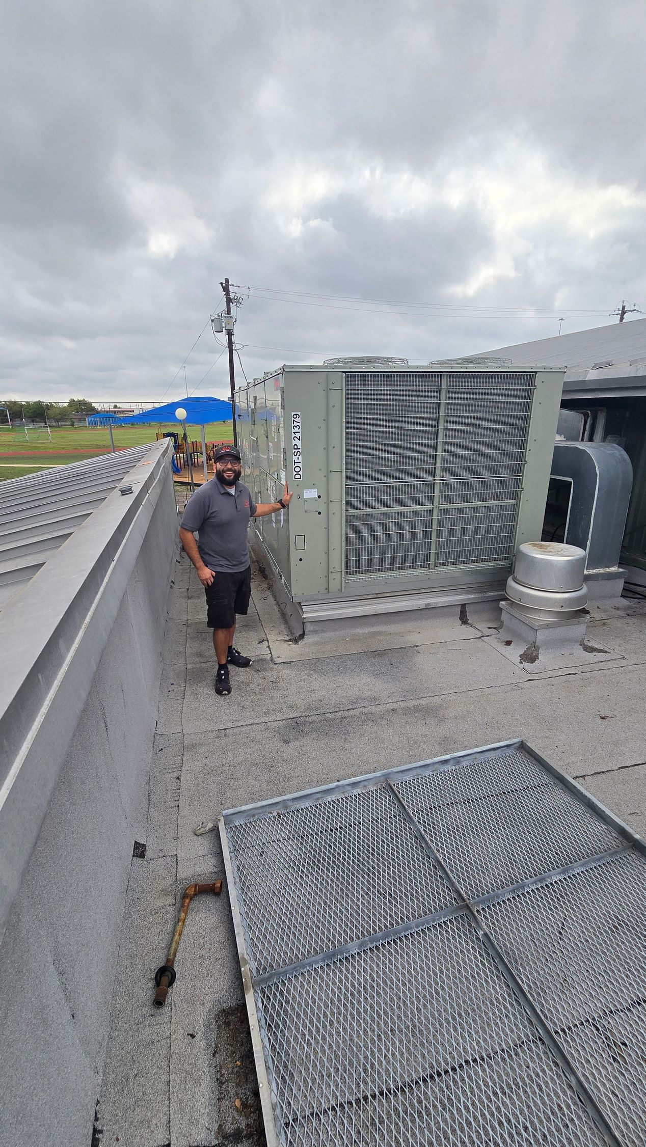 Worker standing beside rooftop HVAC units under a cloudy sky