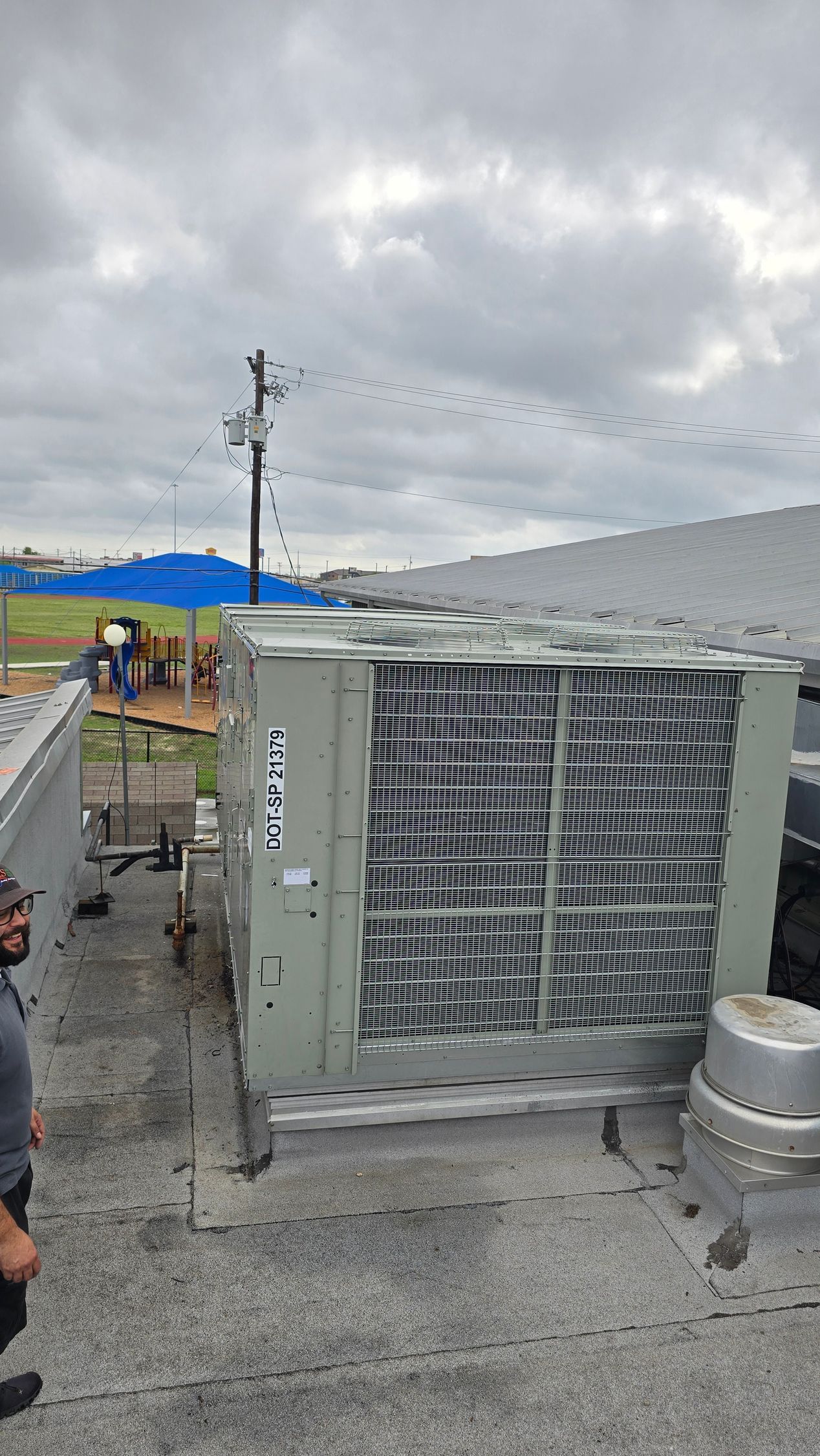 Large outdoor HVAC unit on a rooftop with cloudy sky and utility poles in the background