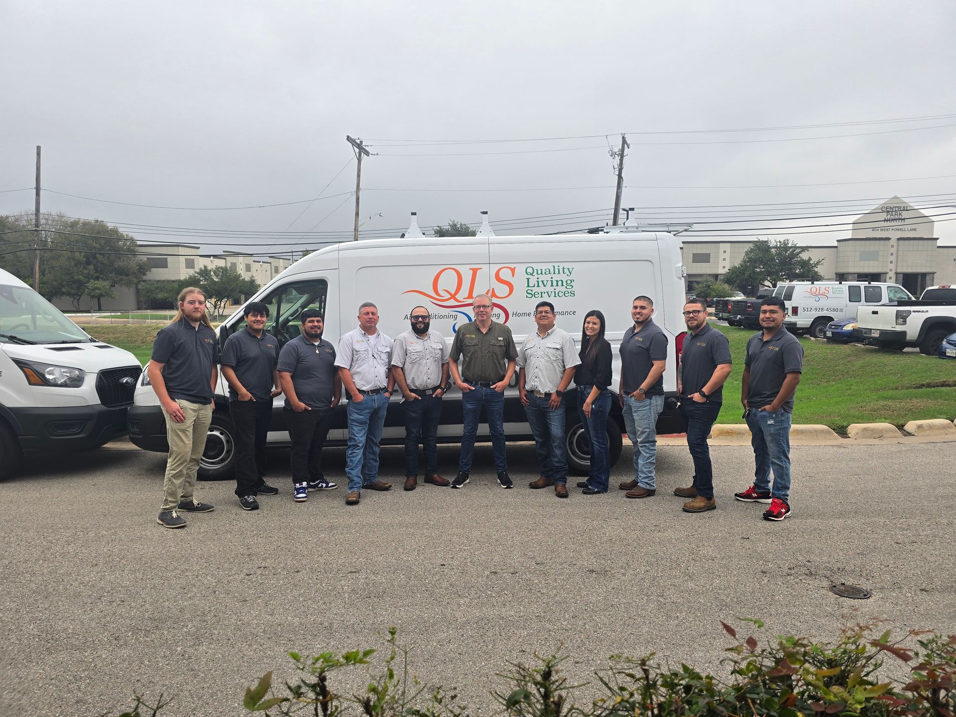Group of people standing in front of a white QLS van in a parking lot under cloudy skies